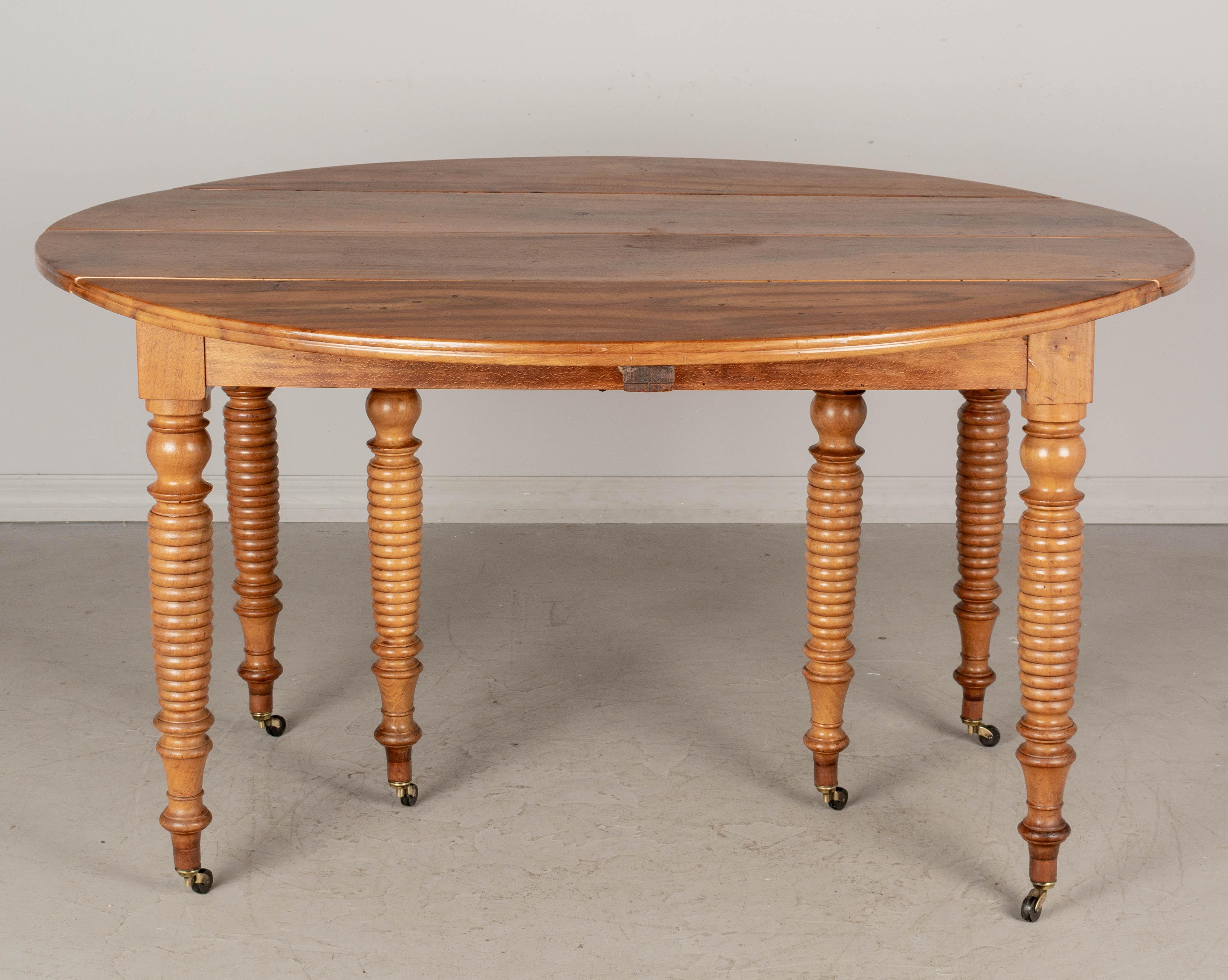 A 19th century French Country Louis Philippe style drop-leaf dining table. Made of walnut with six turned legs on new brass castors. Legs have been lengthened so the table is a good height for dining. Three yellow pine leaves are newer and 19