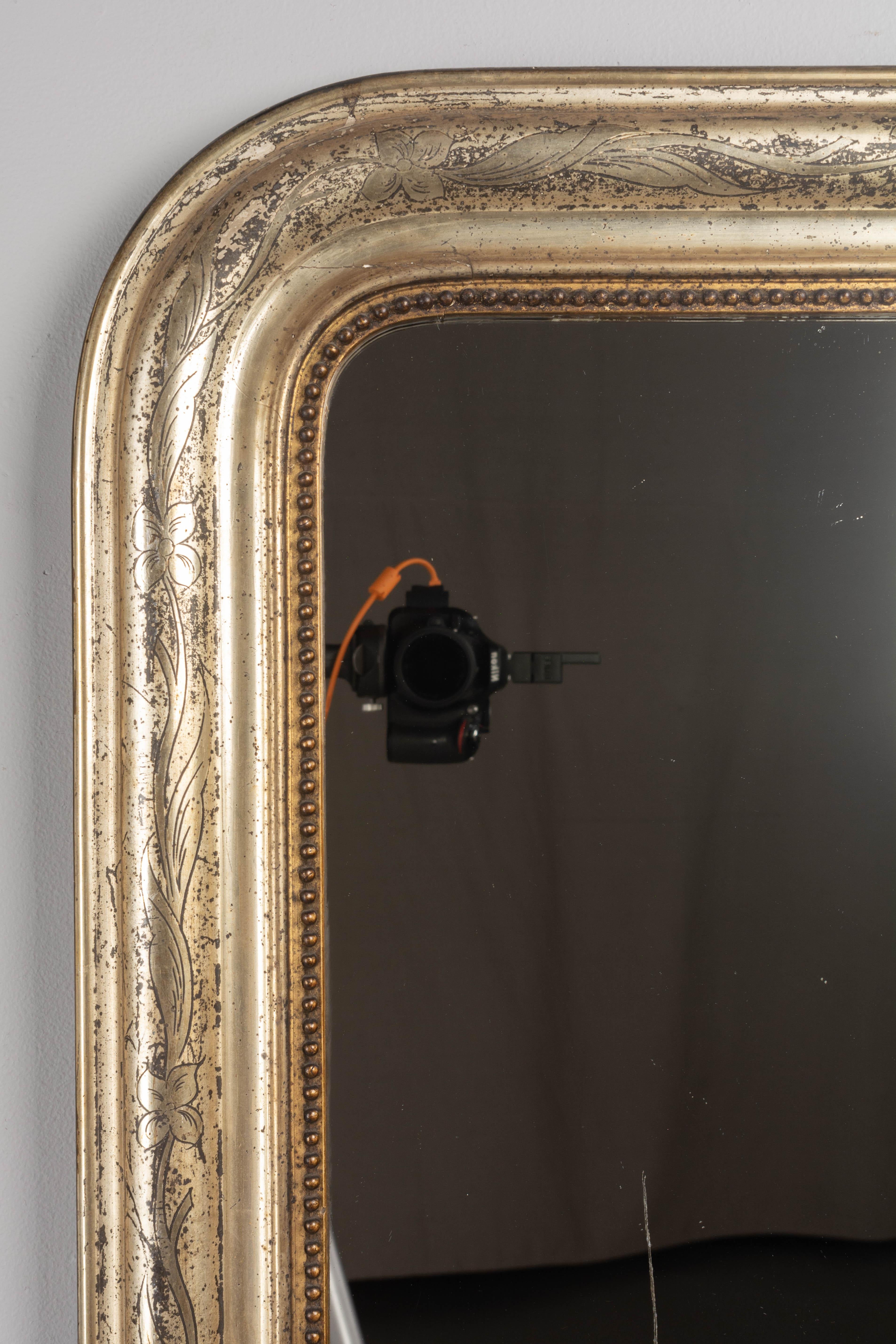 A 19th century French Louis Philippe style gilded mantel mirror with curved top corners, incised decoration and inner bead border. Warm silvery gilt finish with beautiful patina. Minor losses to finish. Original mirror has some scratches. Please