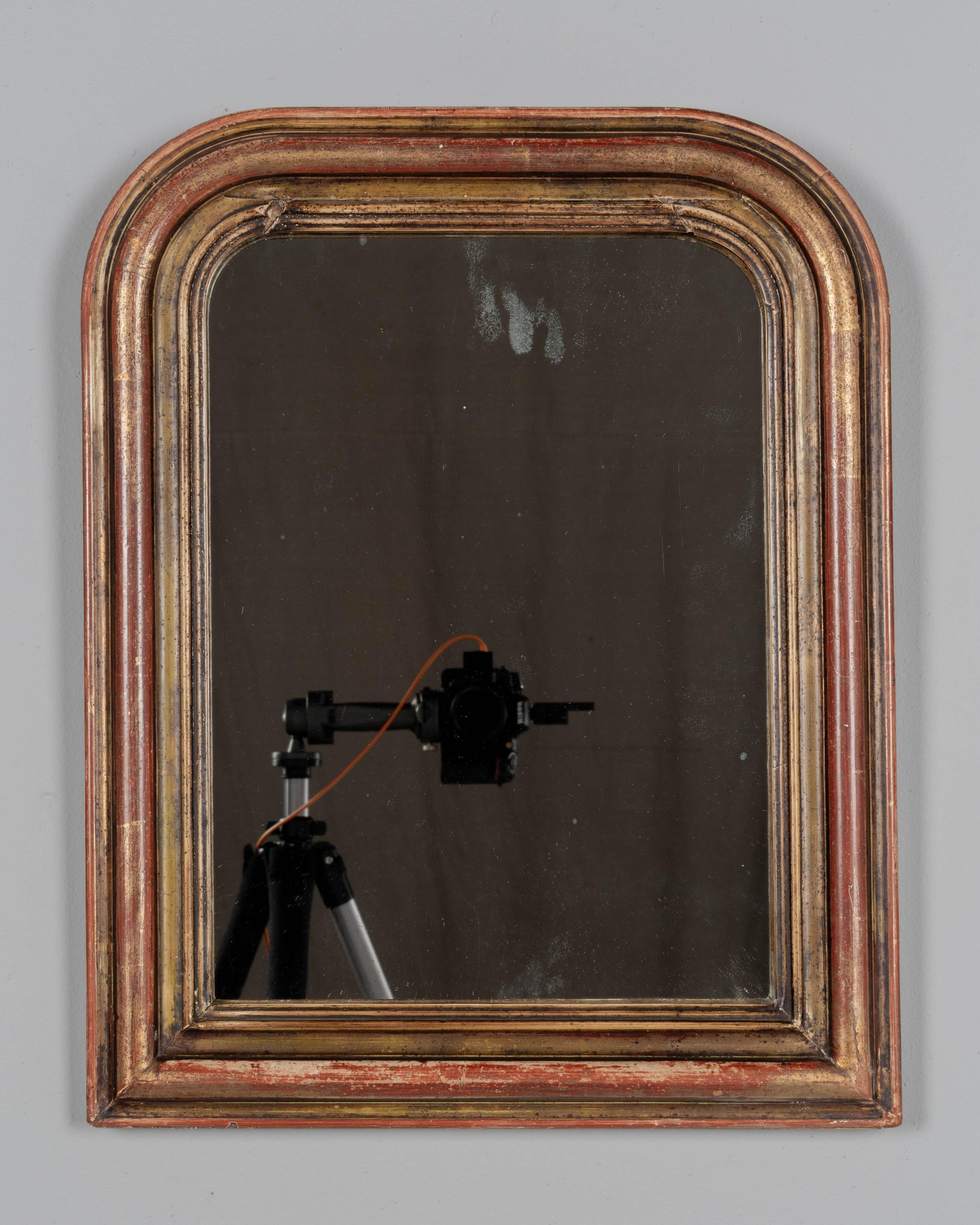 Specchio in stile Louis Philippe del XIX secolo, con angoli superiori curvi e finitura dorata calda con sottofondo rosso. Bella patina con lievi ritocchi alla doratura e riparazione all'angolo inferiore destro. Specchio originale con alcune macchie.