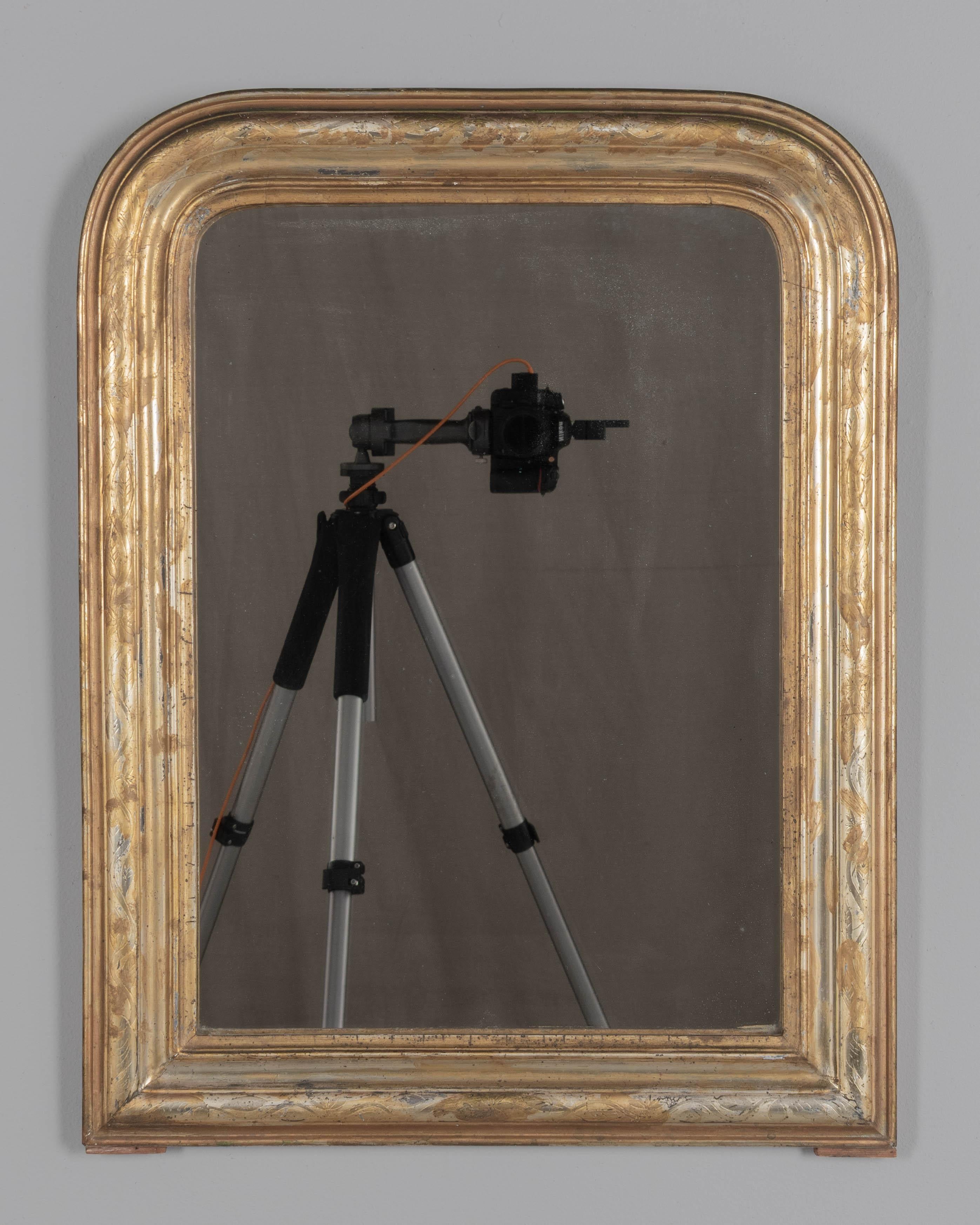 Miroir français du XIXe siècle de style Louis Philippe, avec des angles supérieurs incurvés, un décor de feuilles incisées et une finition argentée et dorée. Miroir d'origine légèrement argenté. Veuillez vous référer aux photos pour plus de détails.