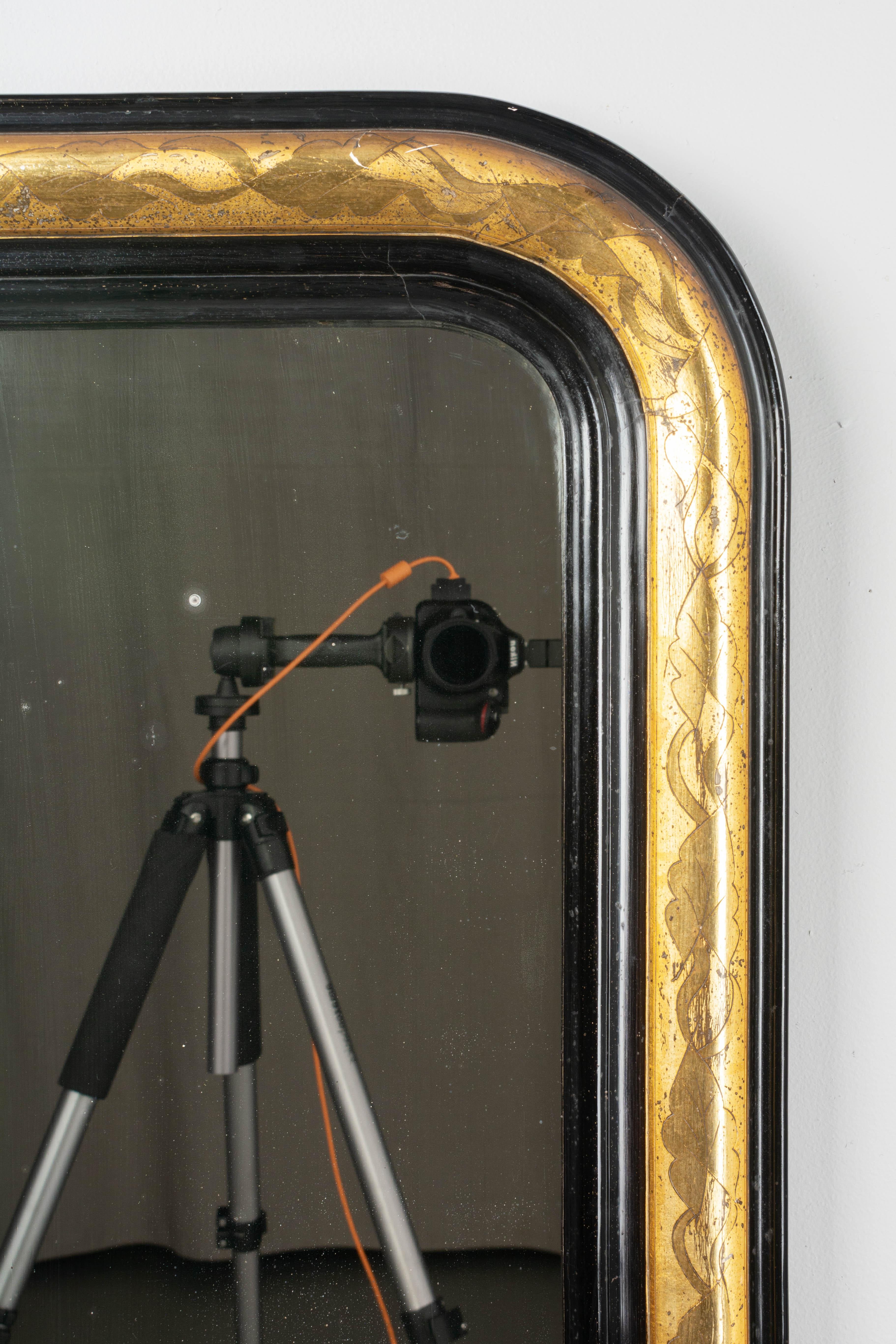 A 19th century Louis Philippe French mirror with curved top corners. Ebonized and gilded finish with incised decoration. In good condition with bright gilt finish. Original mirror with old silvering. Frame has minor repair to bottom