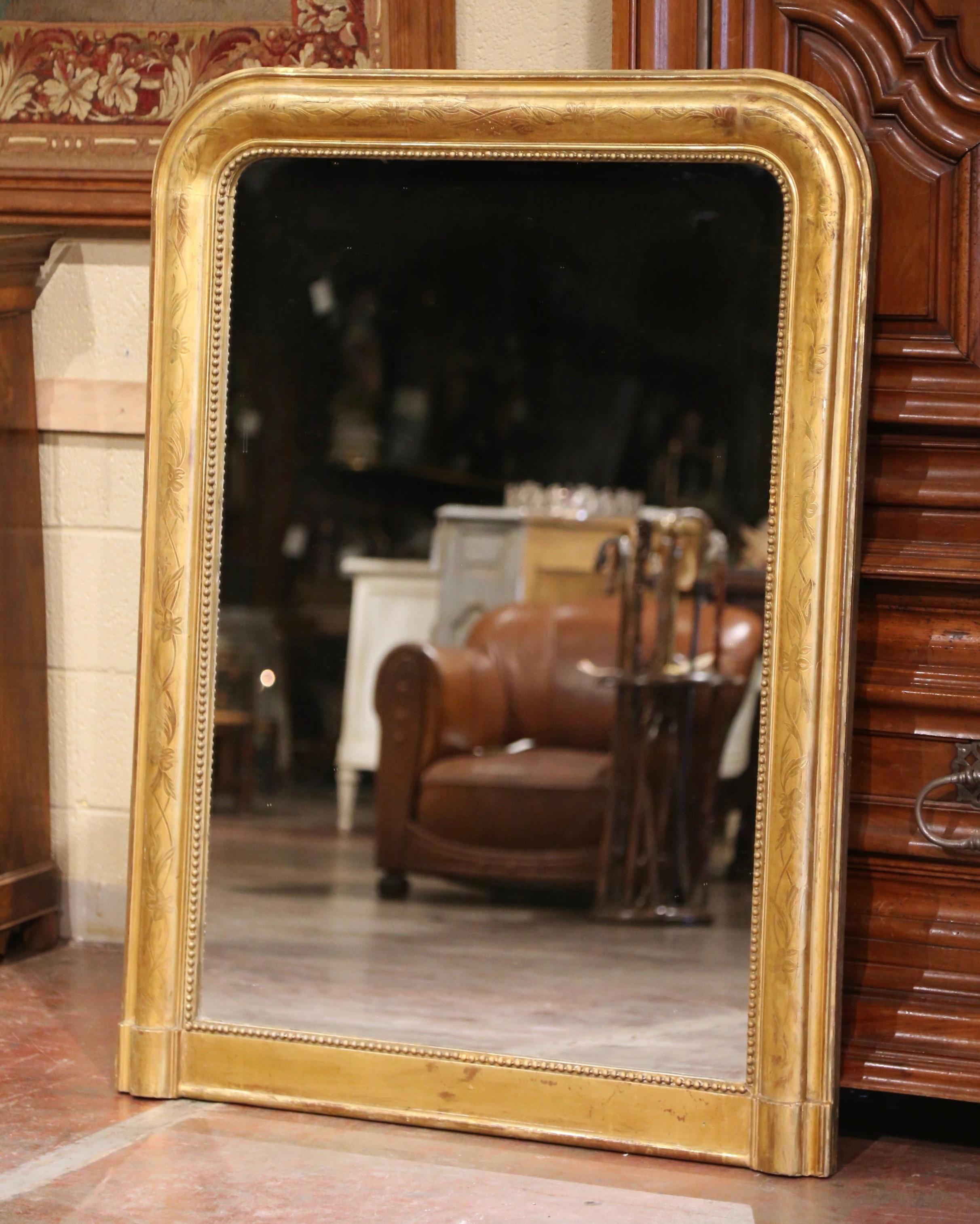 Crafted in the Burgundy region of France circa 1850, the elegant antique mirror has traditional lines with rounded corners at the top and a thick straight plinth form at the bottom. The rectangular frame is decorated with a discrete engraved floral