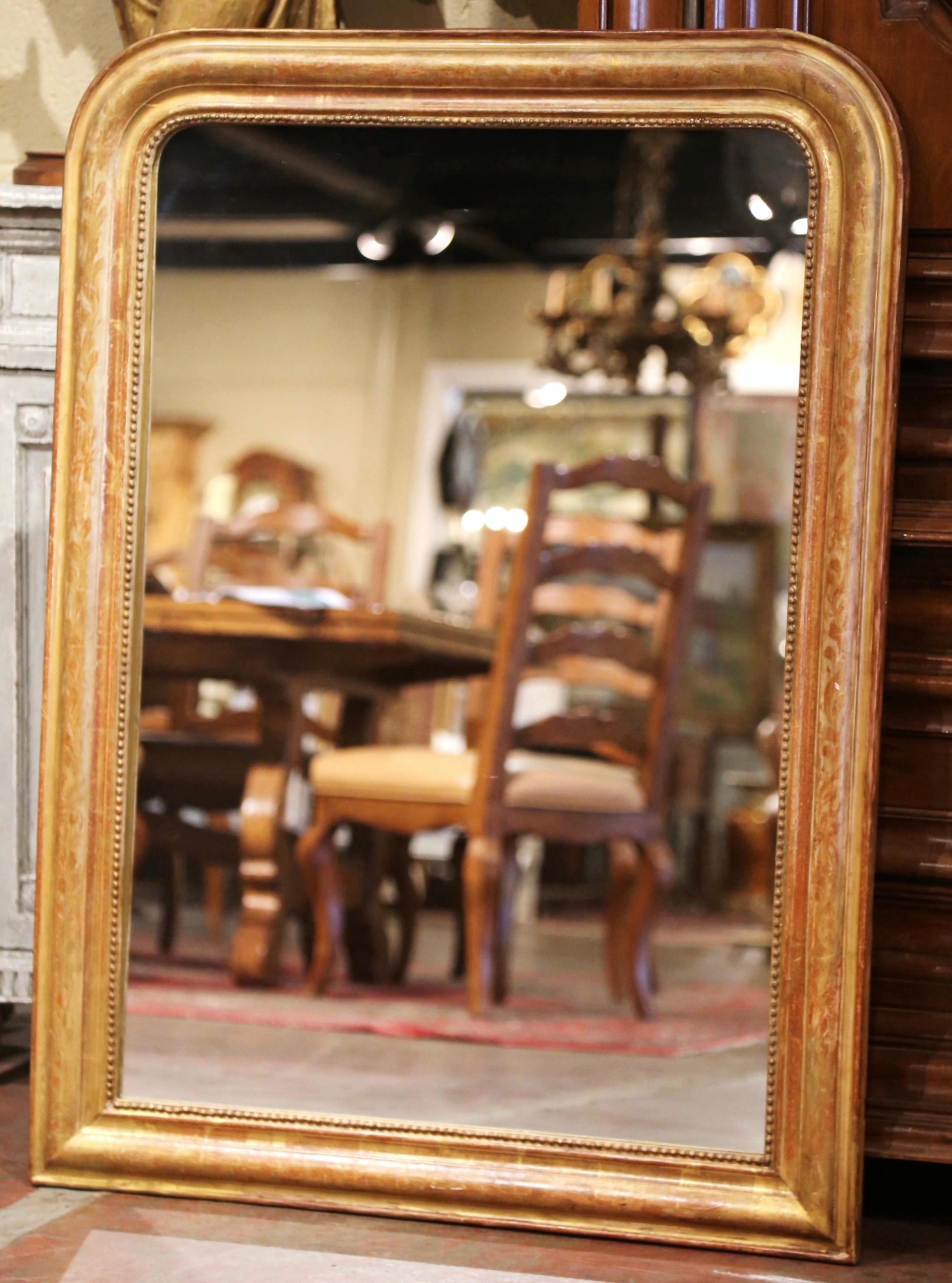 Crafted in the Burgundy region of France circa 1860, the large antique gilt mirror has traditional lines with rounded corners; the rectangular thick frame is decorated with a discrete engraved floral motif throughout and embellished with bead decor