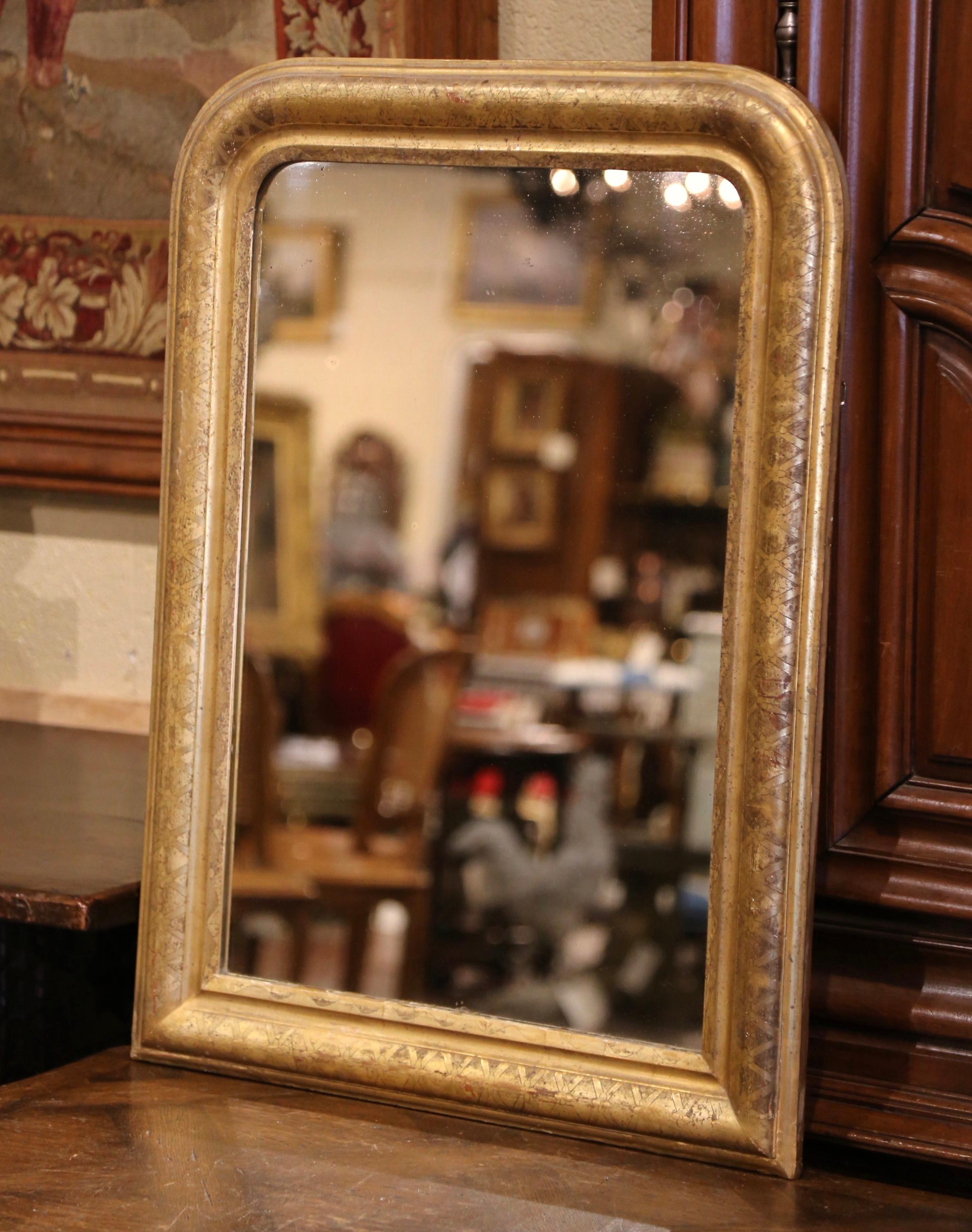 Crafted in the Burgundy region of France circa 1860, the antique gilt mirror has traditional lines with rounded corners; the rectangular frame is decorated with a discrete engraved geometric motif  with multiple X throughout the frame. The wall