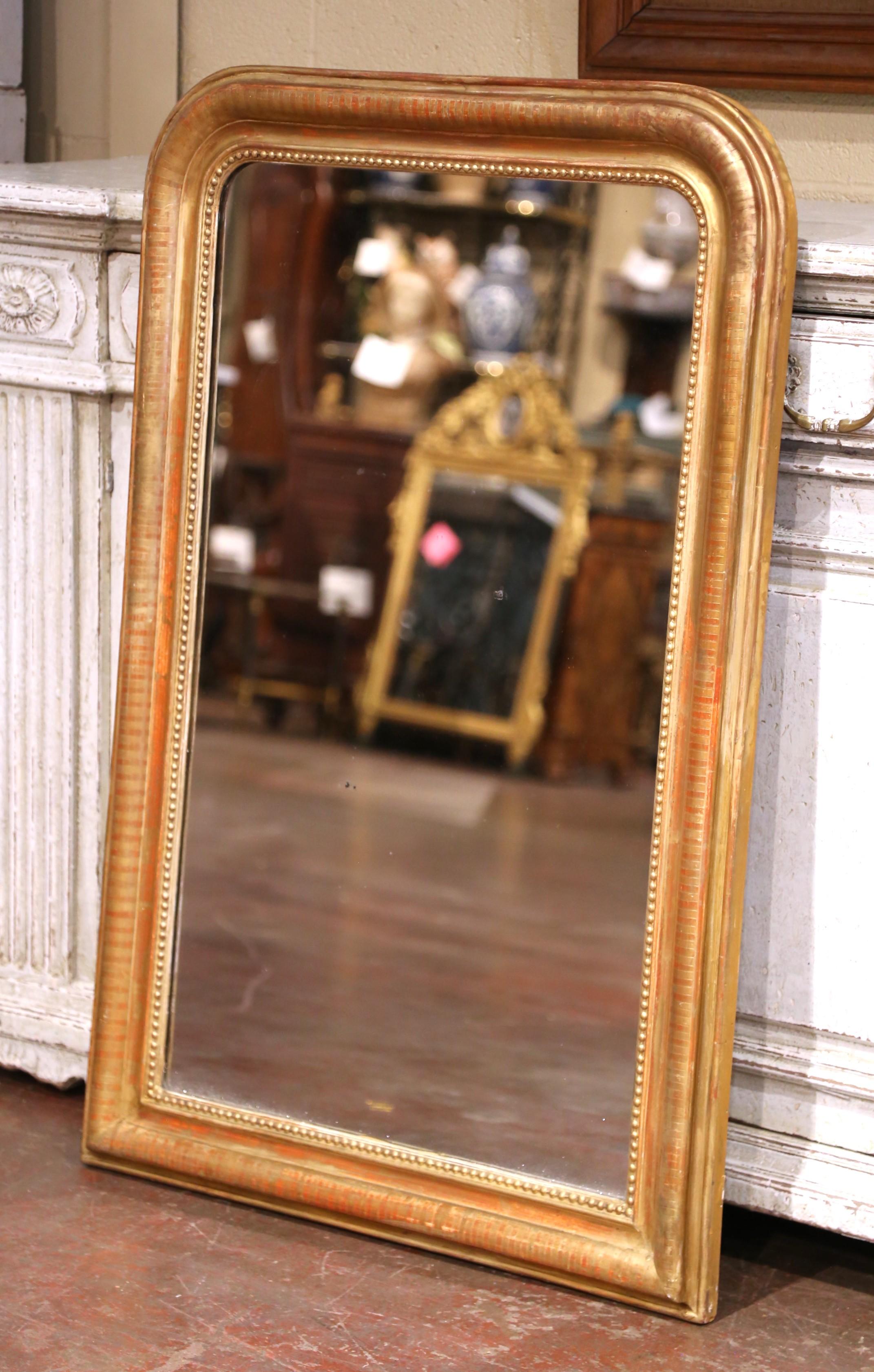 Crafted in the Burgundy region of France circa 1860, the large antique gilt mirror has traditional lines with rounded corners; the rectangular thick frame is decorated with a discrete engraved stripe motif throughout and embellished with bead decor