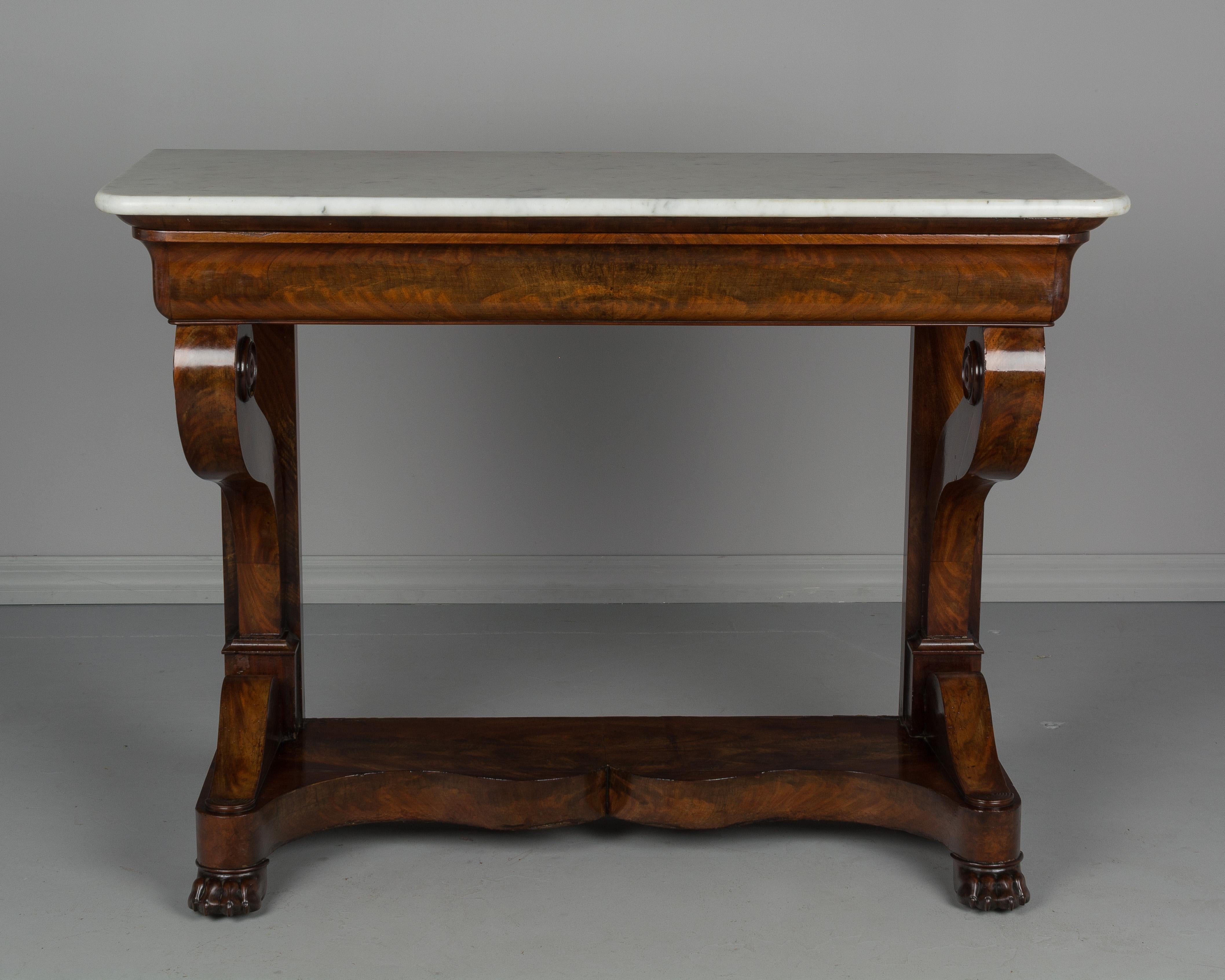 An early 19th century French Louis-Philippe period console made of bookmatched veneer of flame mahogany with oak as a secondary wood. Sculptural front legs ending in scrolls and resting on a plinth base with curved front and lion's paw feet.