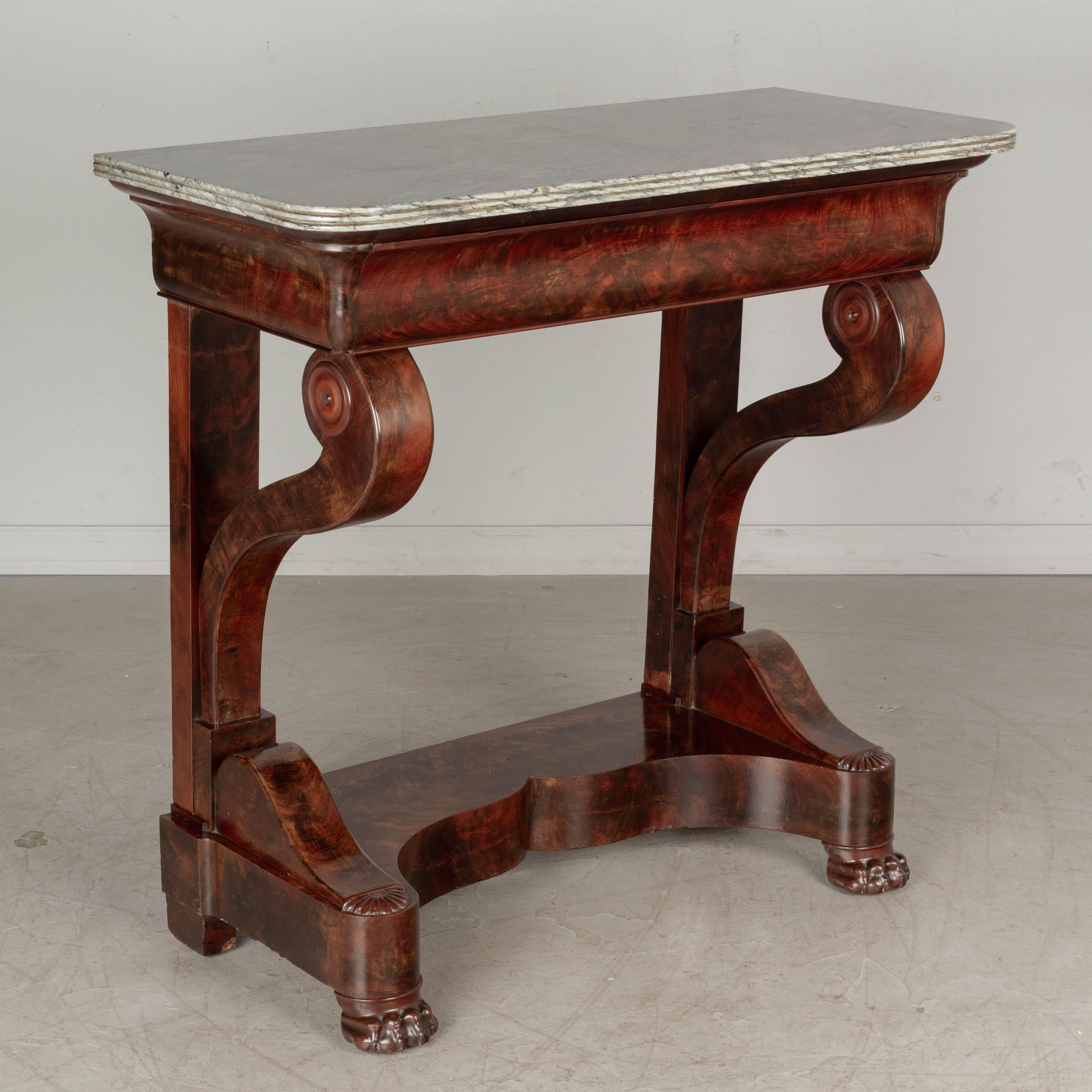 A 19th century French Louis Philippe style console made of book matched veneer of flame mahogany with dovetailed drawer. Sculptural scroll supports resting on a curved plinth base with lion's paw feet. Original gray veined marble top with rounded