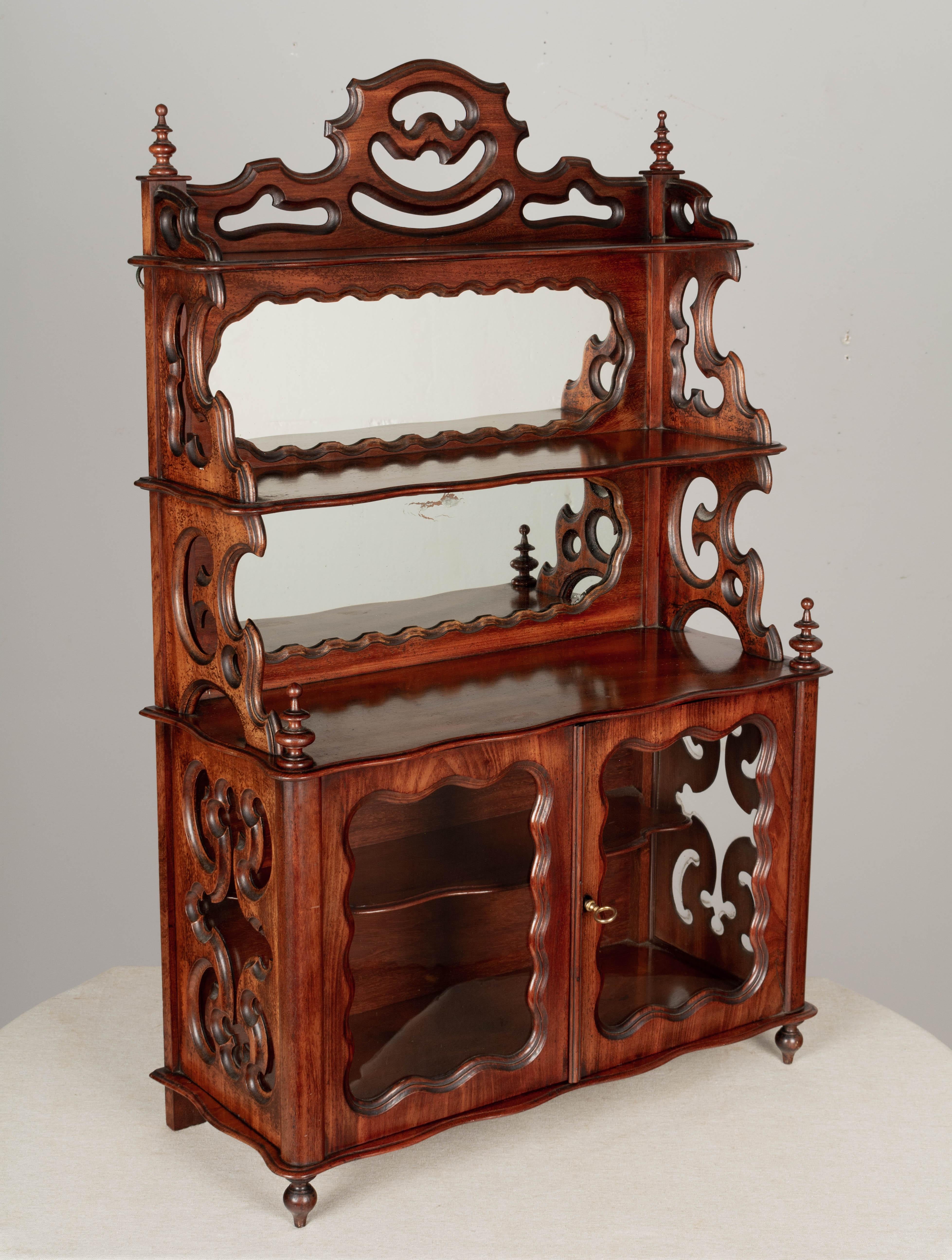 A 19th century French Louis Philippe style vitrine or miniature buffet, made of solid mahogany with glass cabinet doors and mirror backed tiered shelves. Glass cabinet door opens to one shelf. Working lock and key, missing escutcheon. Beautifully