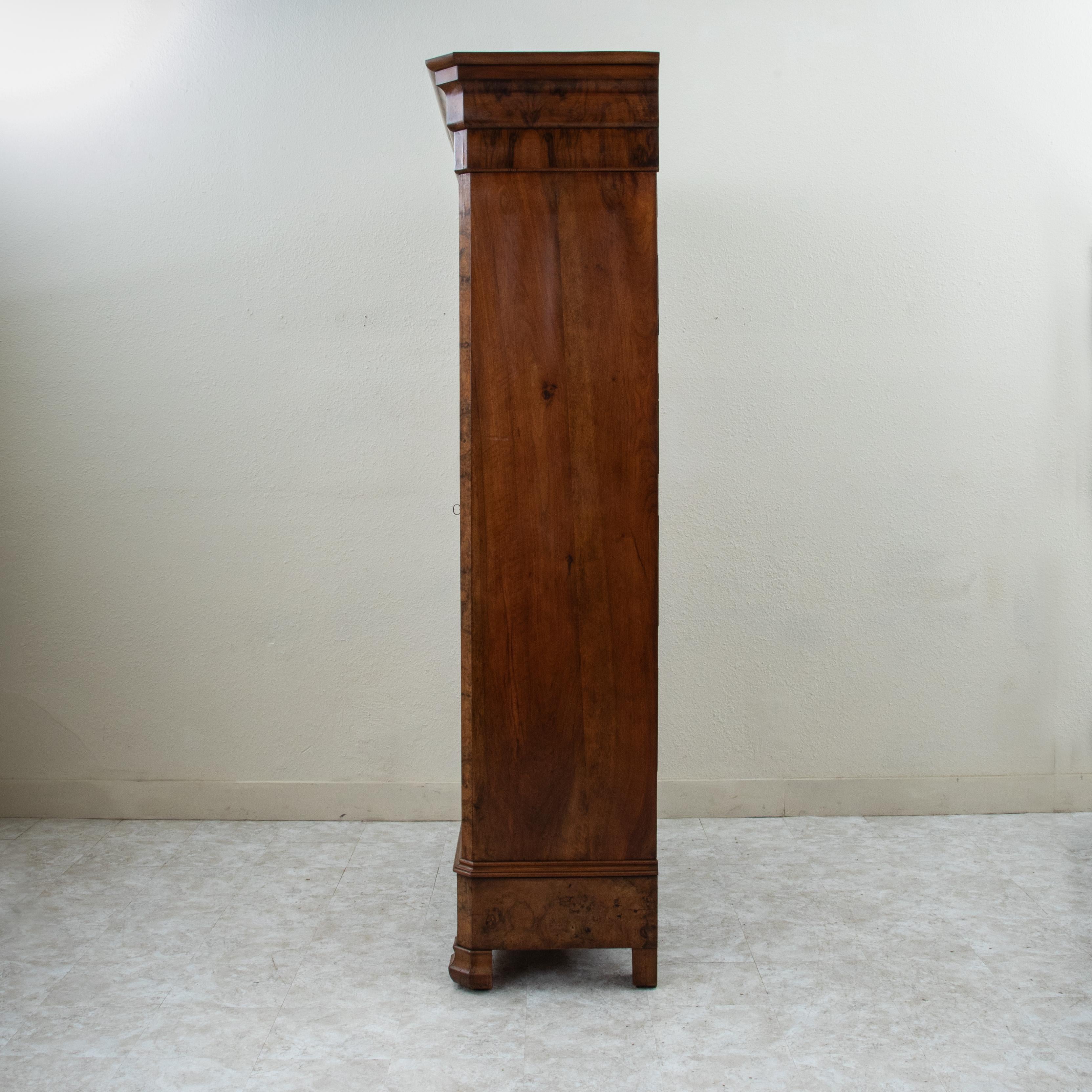 Standing at nearly eight feet in height, this impressive nineteenth century French Louis Philippe period armoire features a facade of exquisite book matched burl walnut and solid paneled sides. Its two doors open to reveal an interior with two