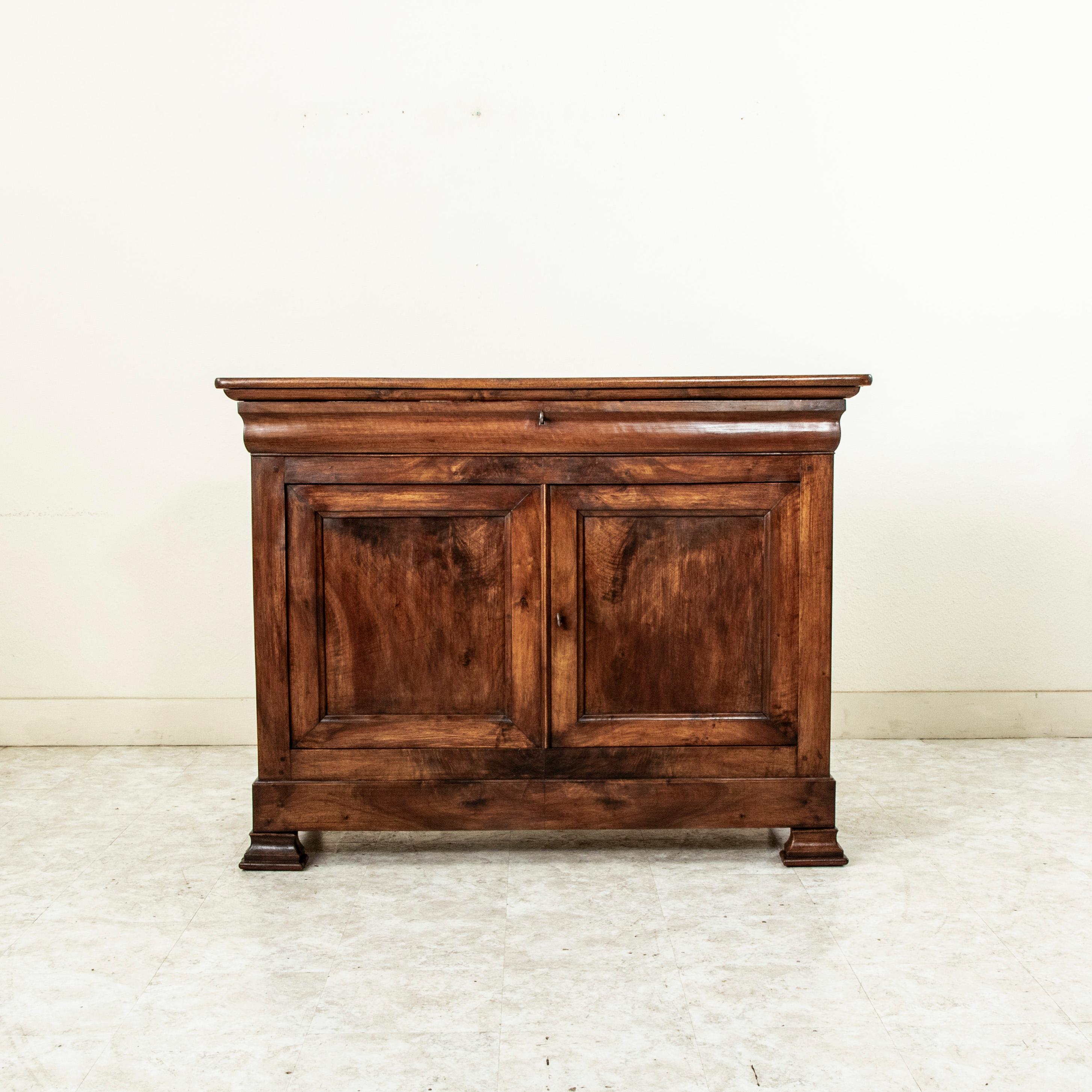 This French Louis Philippe period buffet from the nineteenth century is constructed of solid walnut and features a book matched facade. A single upper drawer fits seamlessly into the apron and two lower doors open to allow access to the large cavity