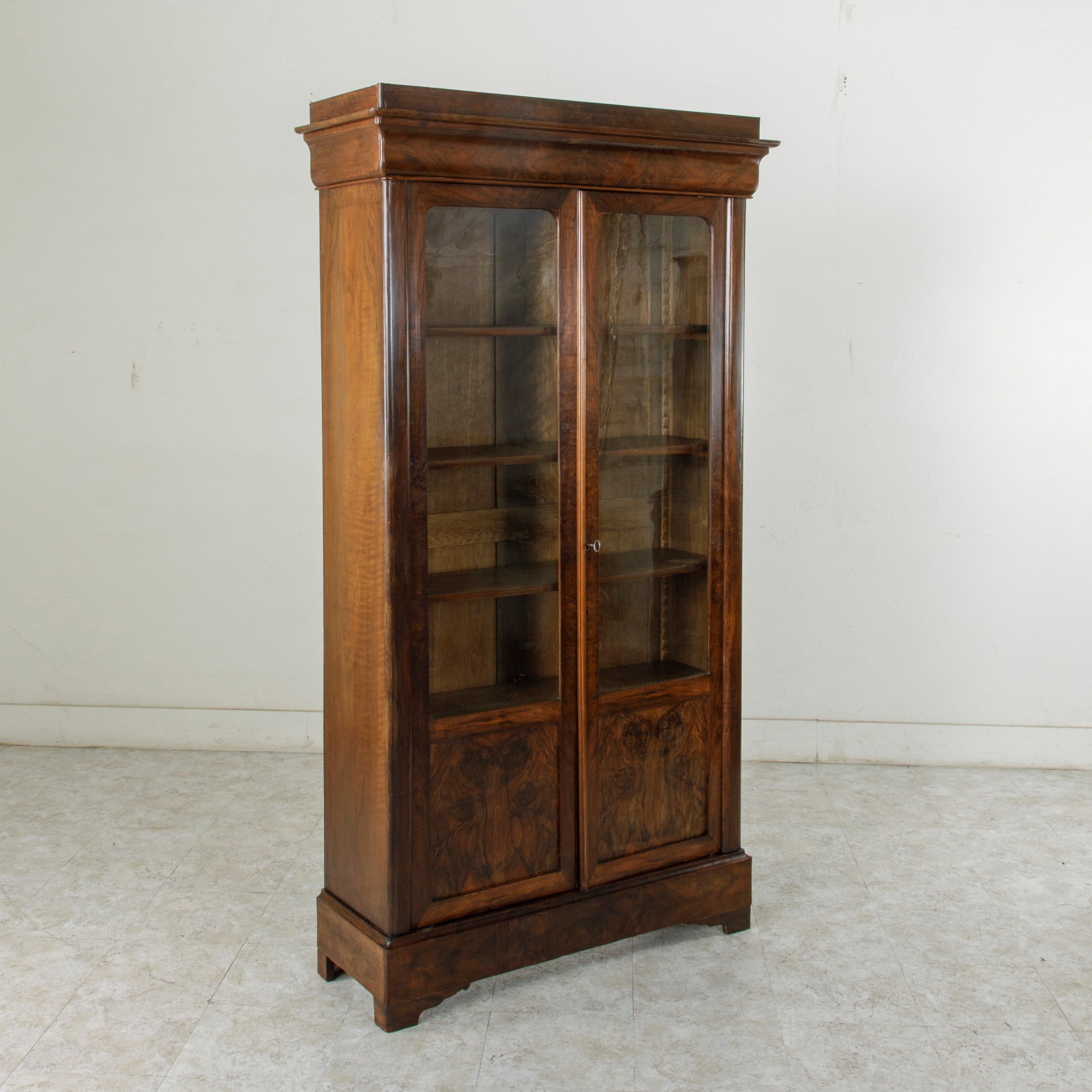 This 19th century Louis Philippe period flamed mahogany bibliothèque, bookcase, or vitrine features a book matched burl facade with simple, handsome lines and two doors inset with their original hand blown glass. It has five adjustable interior