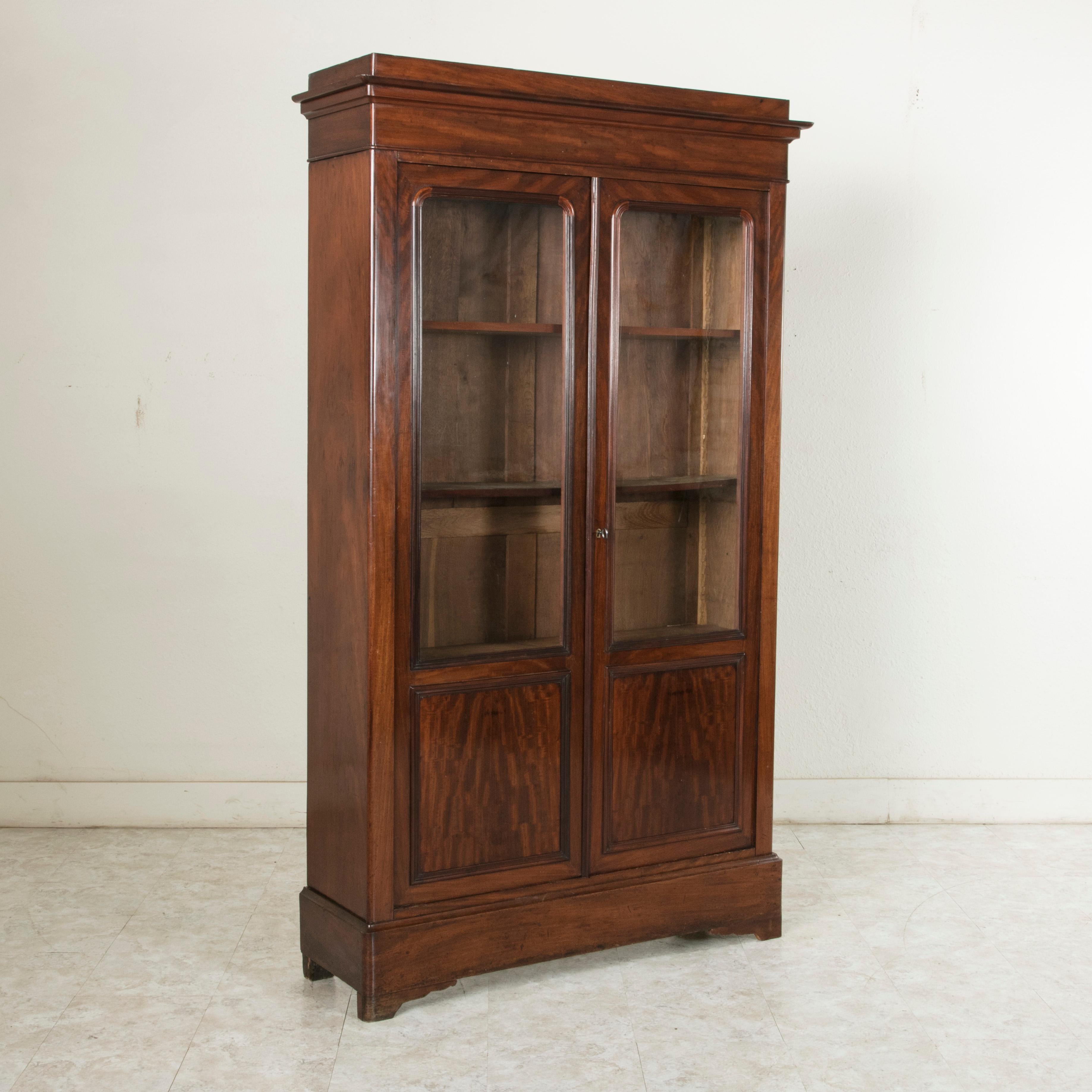 This 19th century Louis Philippe period bookcase or vitrine features a mahogany facade with simple, handsome lines and two doors inset with their original hand blown glass. It has three adjustable interior shelves for ample storage and display