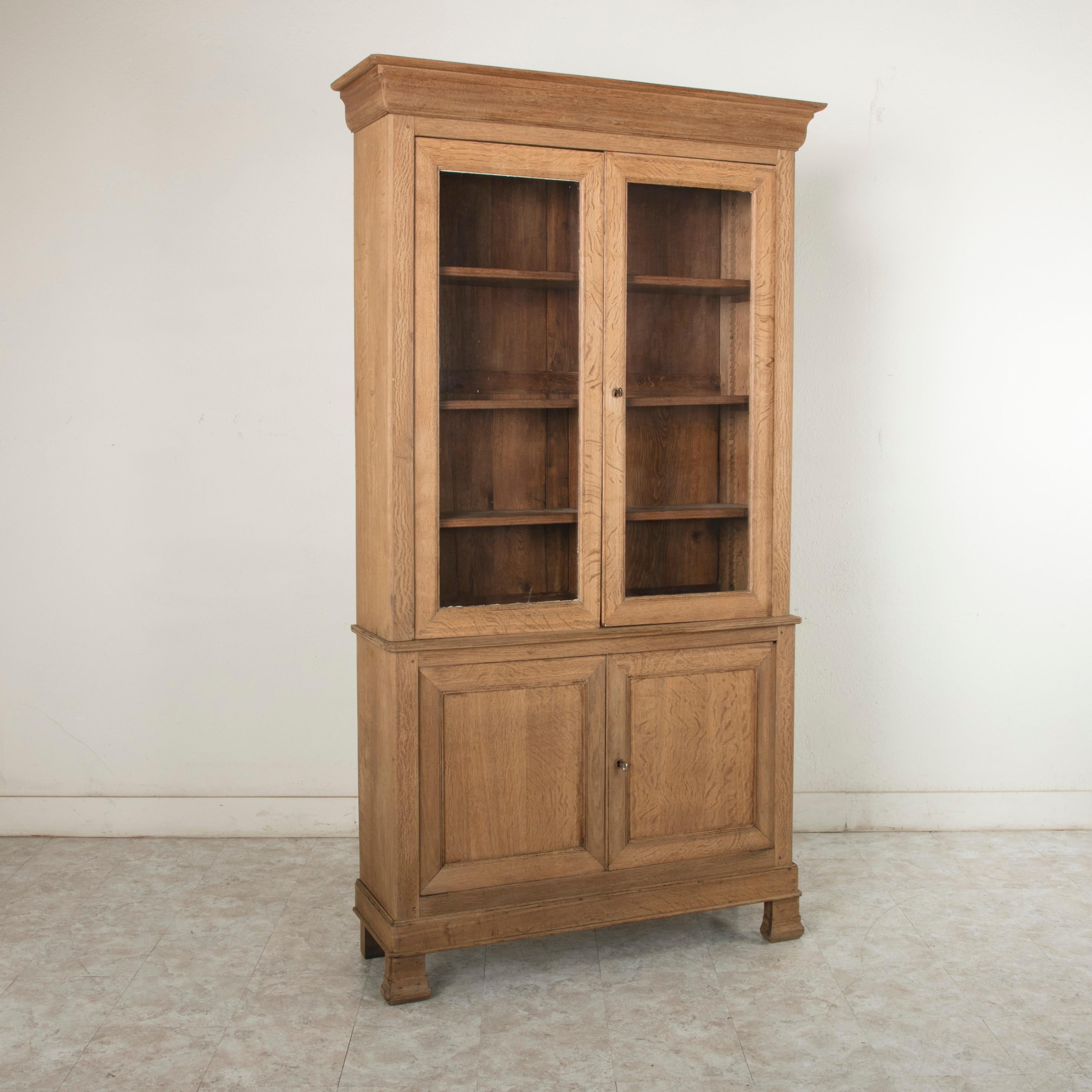 This French Louis Philippe period oak buffet deux corps bookcase from the 19th century features a closed lower cabinet with two doors and an upper cabinet with its original hand blown glass doors. The glass displays beautiful waves and bubbles.