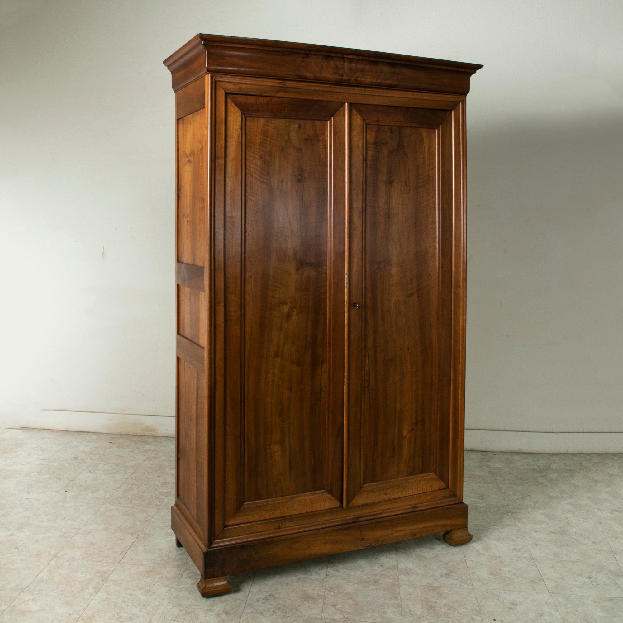 This 19th century armoire is constructed of solid walnut and features simple clean lines, the Classic distinction of the Louis Philippe style. A period piece, its solid paneled sides and doors glow with the rich patina of the walnut. The two doors