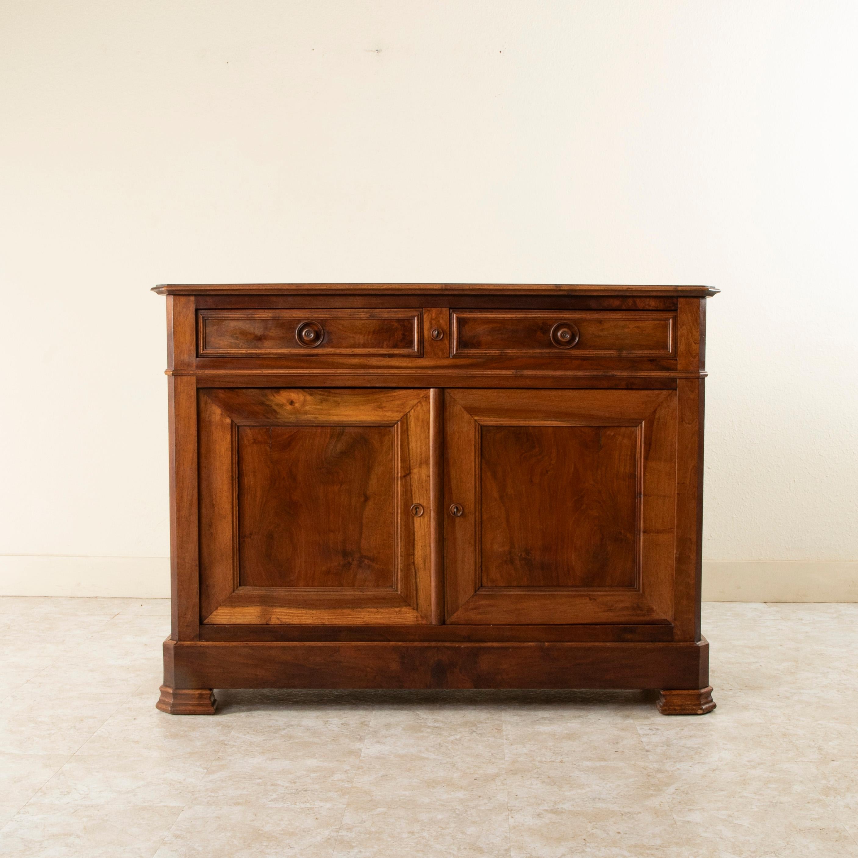 This small scale Louis Philippe period buffet from the nineteenth century is constructed of solid walnut. It features two drawers of dovetail construction that fit seamlessly into the apron and two lower doors that open wide to allow access to the
