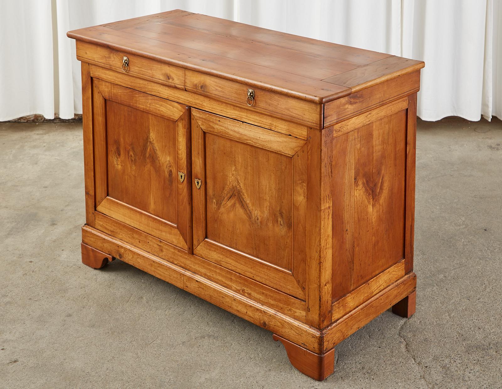 Handsome early 19th century French Louis Philippe period sideboard cabinet, or buffet server. Crafted from radiant grained fruitwood with excellent joinery and craftsmanship. The top of the case has two fitted storage drawers with brass lions head