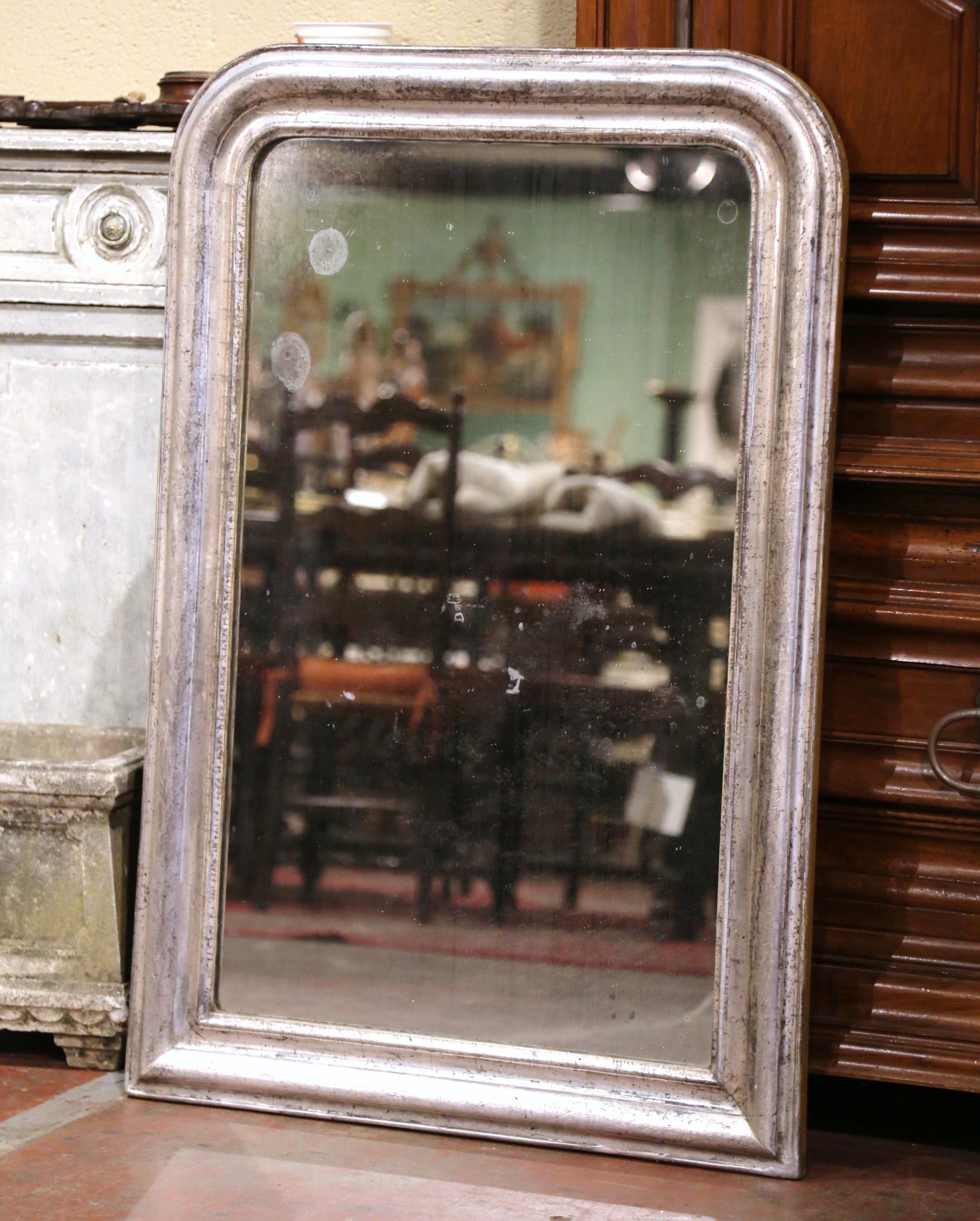 Crafted in the Burgundy region of France, circa 1870, the rectangular antique mirror has traditional, timeless lines with rounded corners. The frame is decorated with a luxurious silver leaf finish over discrete engraved floral motifs. The classic