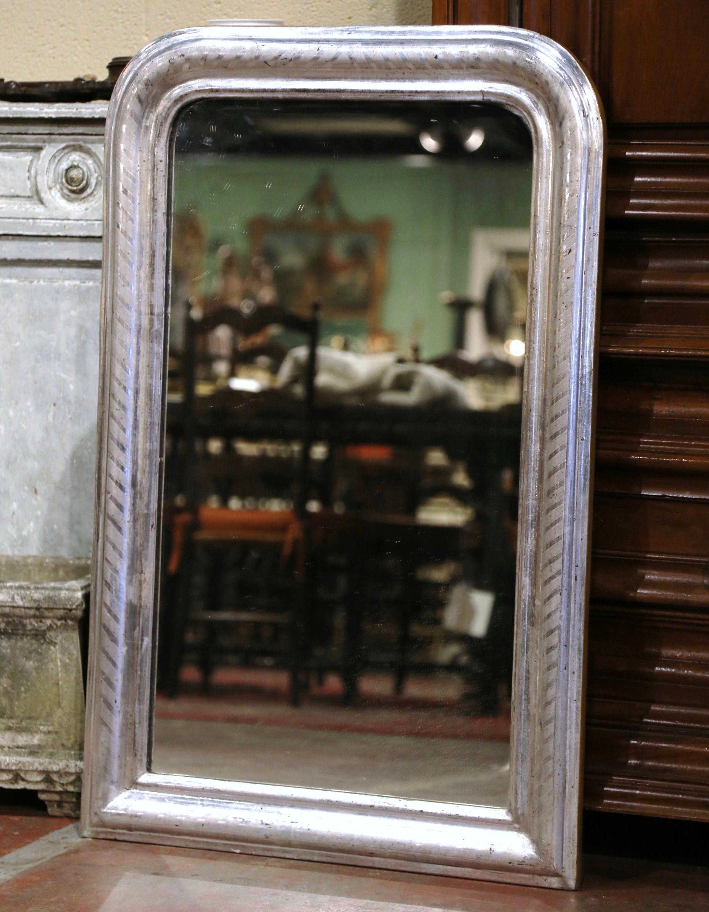 Crafted in the Burgundy region of France, circa 1870, and rectangular in shape, the elegant antique mirror has traditional, timeless lines with rounded corners. The frame is decorated with a luxurious silver leaf finish over discrete engraved