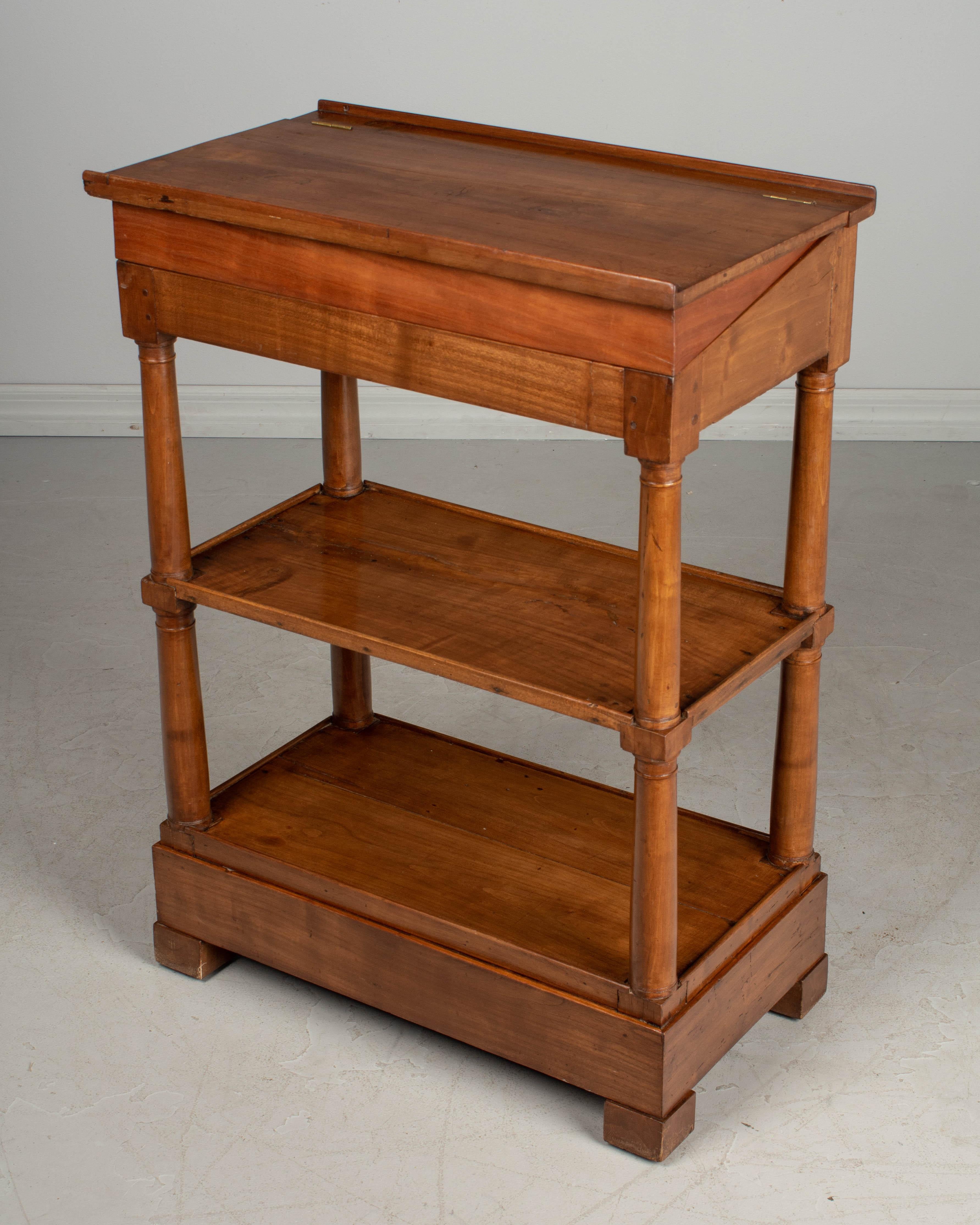 A 19th century French Louis Philippe small étagère, or bookcase, made of solid cherrywood with turned columns and finished on all sides. The top is hinged and has a shallow storage compartment. This was originally a slant top Stand. A removable