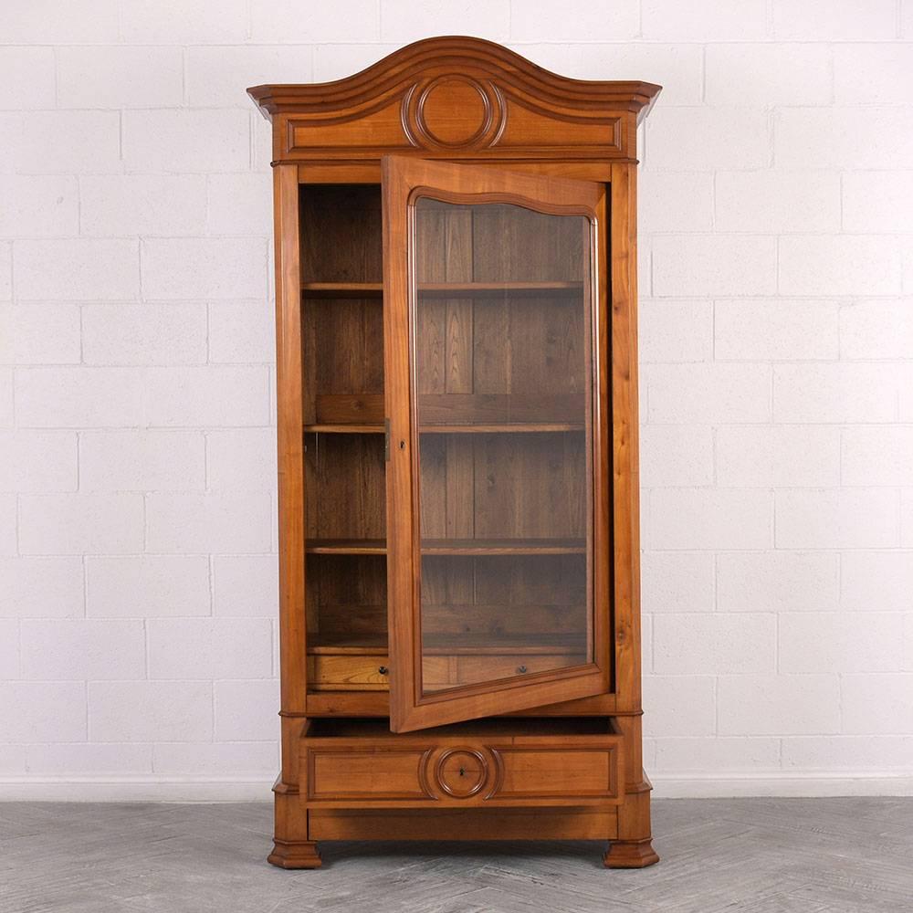 This 1870s French Louis Philippe-style bookcase is made of solid walnut wood with the original stain and a beautiful natural patina and polished finish. The carved mouldings accent the crown and bottom drawer with a cornice overhang and decorative