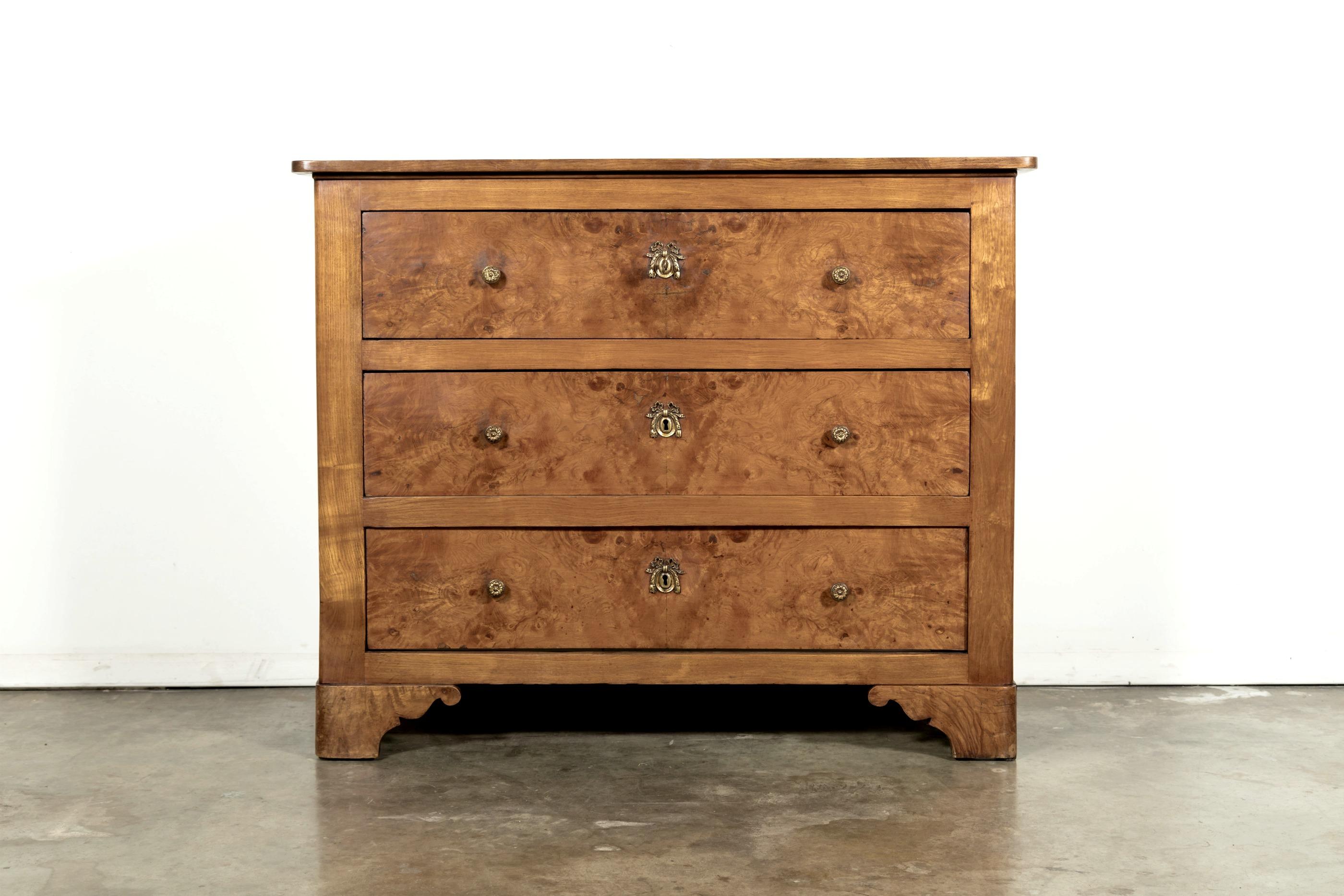 A handsome French Louis Philippe style commode handcrafted of solid chestnut with a bookmatched burled chestnut front. Featuring three fitted long drawers resting upon shaped pistolet feet. Each drawer having a pair of circular pulls with a center
