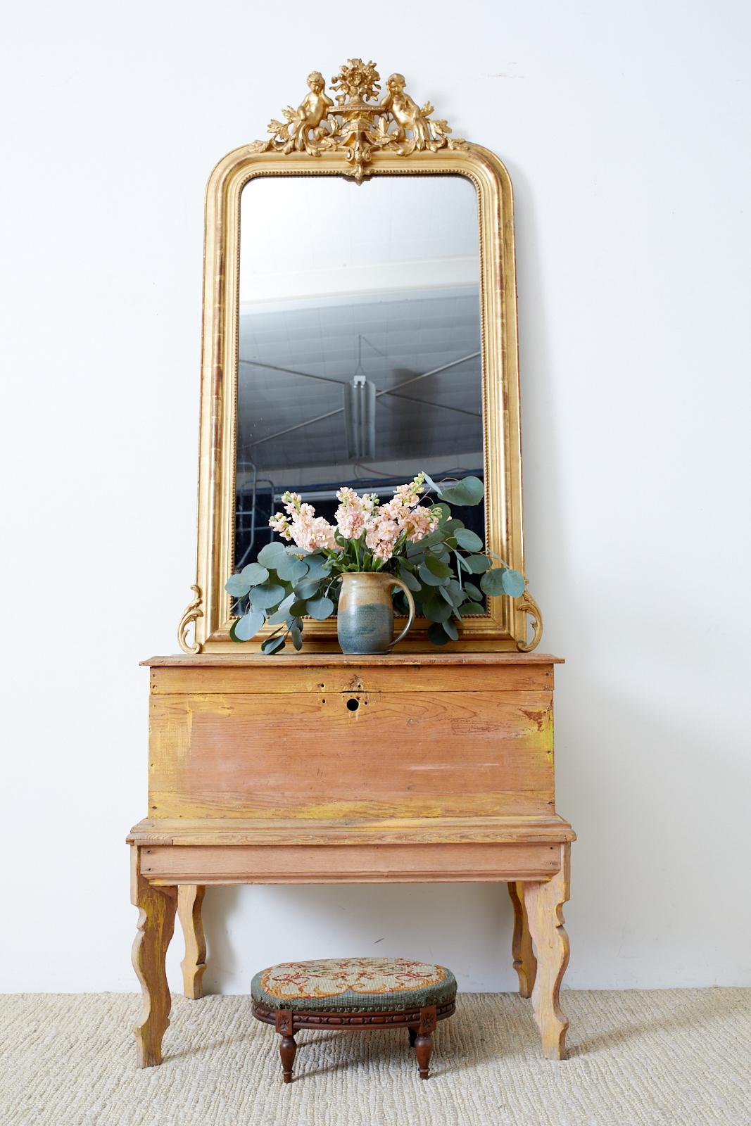 Grand 19th century giltwood mirror made in the French Louis Philippe taste. Features a distinctive gesso crest centered by an urn with floral sprays. Flanked on each side are beautiful cherub figures resting on the urn adorned with acanthus. The
