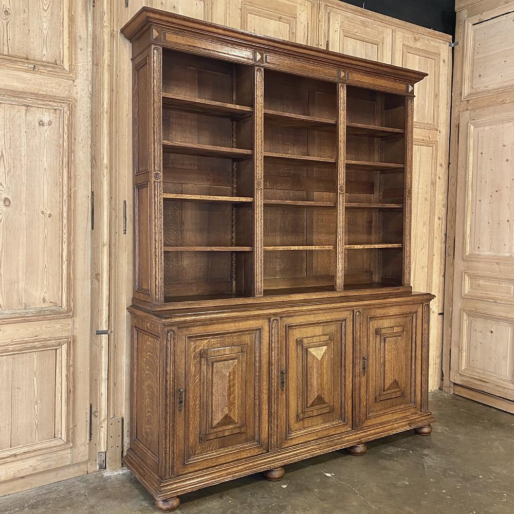 19th century French Louis XIII bookcase was handcrafted from solid oak, and features amazing storage in the adjustable open bookshelf tier on top, separated into three compartments divided by partitions carved with fletching, as well as a massive