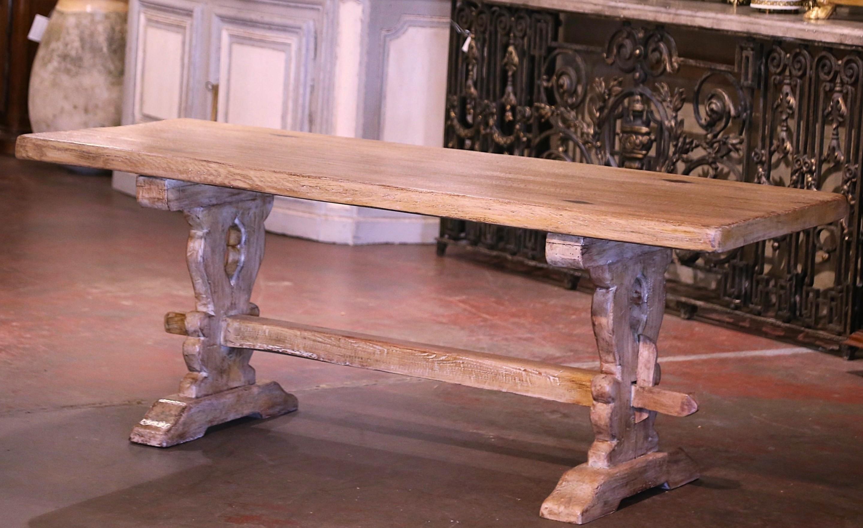 This elegant antique farm table was crafted in Normandy, France circa 1870. Built of solid oak, and almost 7 feet in length, the table stands on carved trestle support legs ending with molded shoe feet, and joined together with a cross bottom