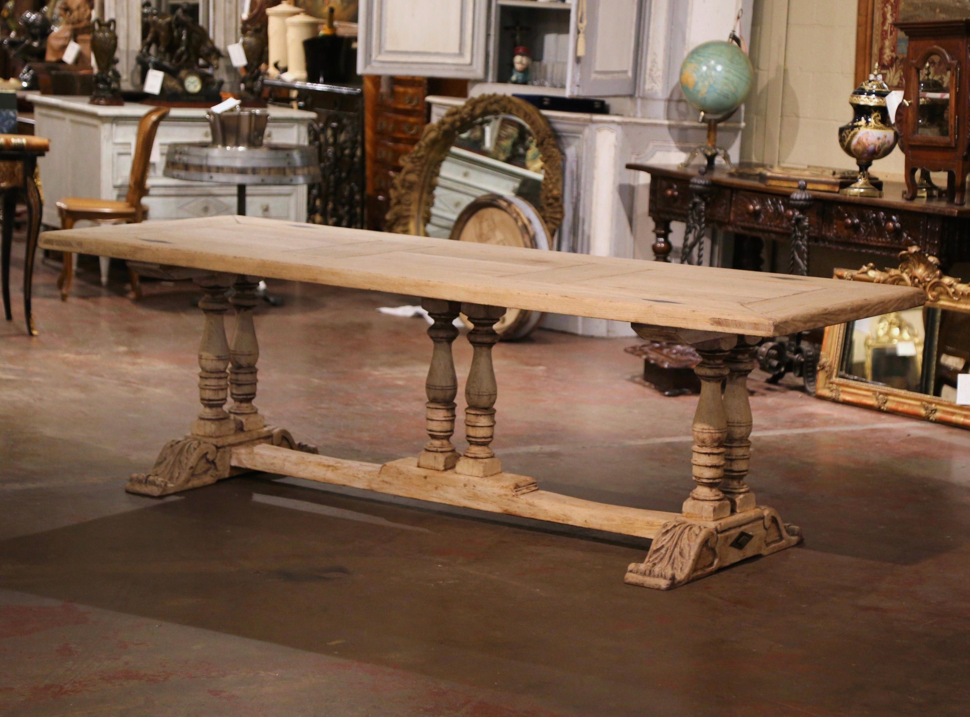 This elegant antique dining table was crafted in Normandy, France circa 1870. Built of solid oak, the table stands on three turned double-baluster support legs joined by cross stretcher; each shoe base is further embellished with hand carved