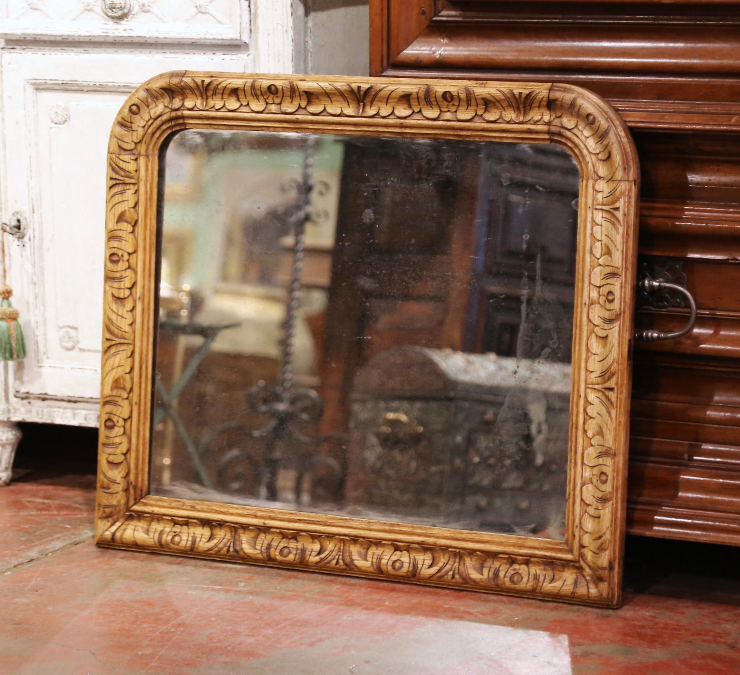 Crafted in France circa 1870, and built of oak wood, the antique mirror is rectangular in shape with rounded corners. The wall decor features a center mirror with mercury glass, and is decorated with hand carved acanthus leaf motifs throughout. The