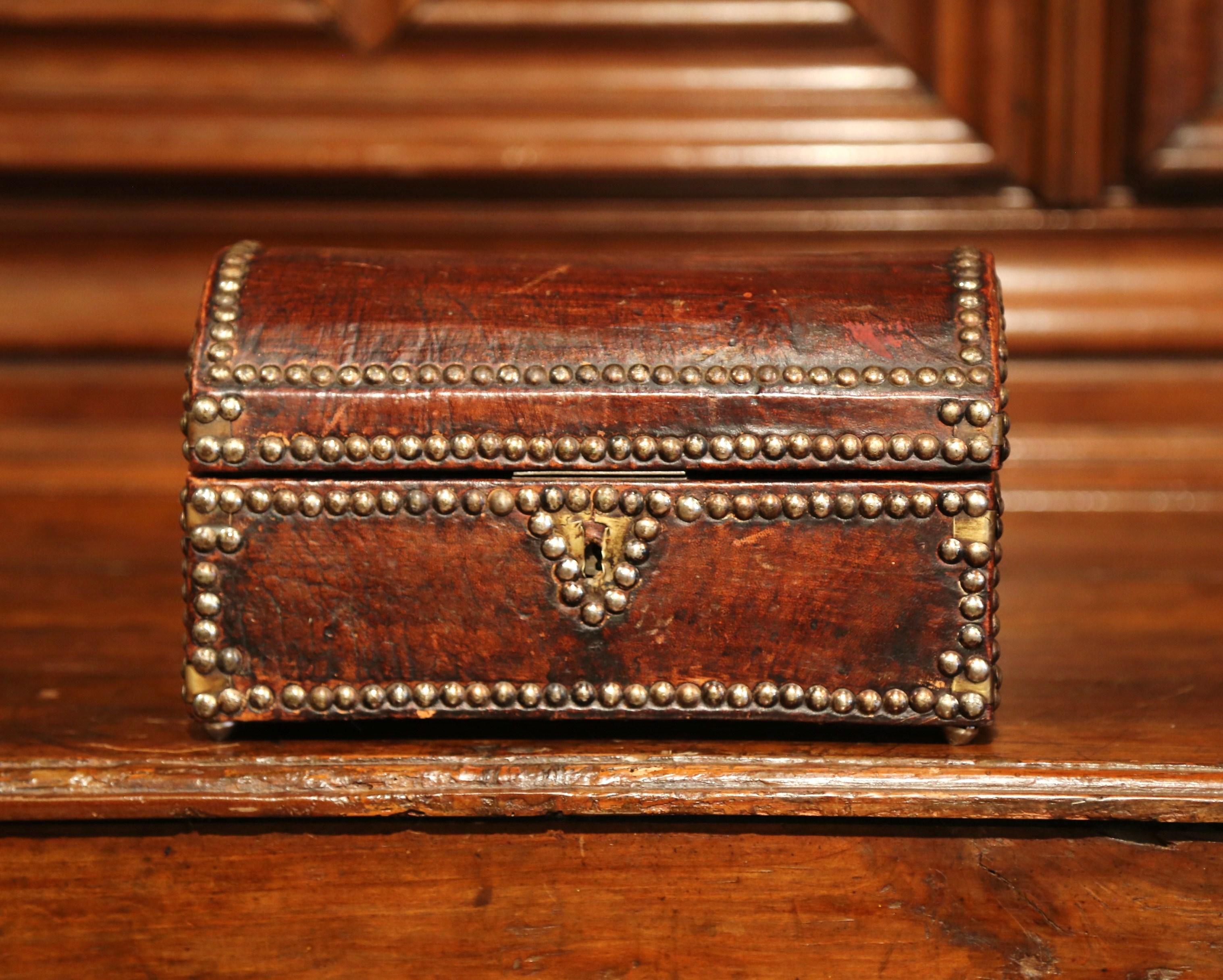 Decorate a shelf or a desk with this beautiful antique trunk from southern France; crafted circa 1850, the brown leather box sits on four round brass feet, and is shaped like a classic storage trunk with an arched top and a rectangular front and