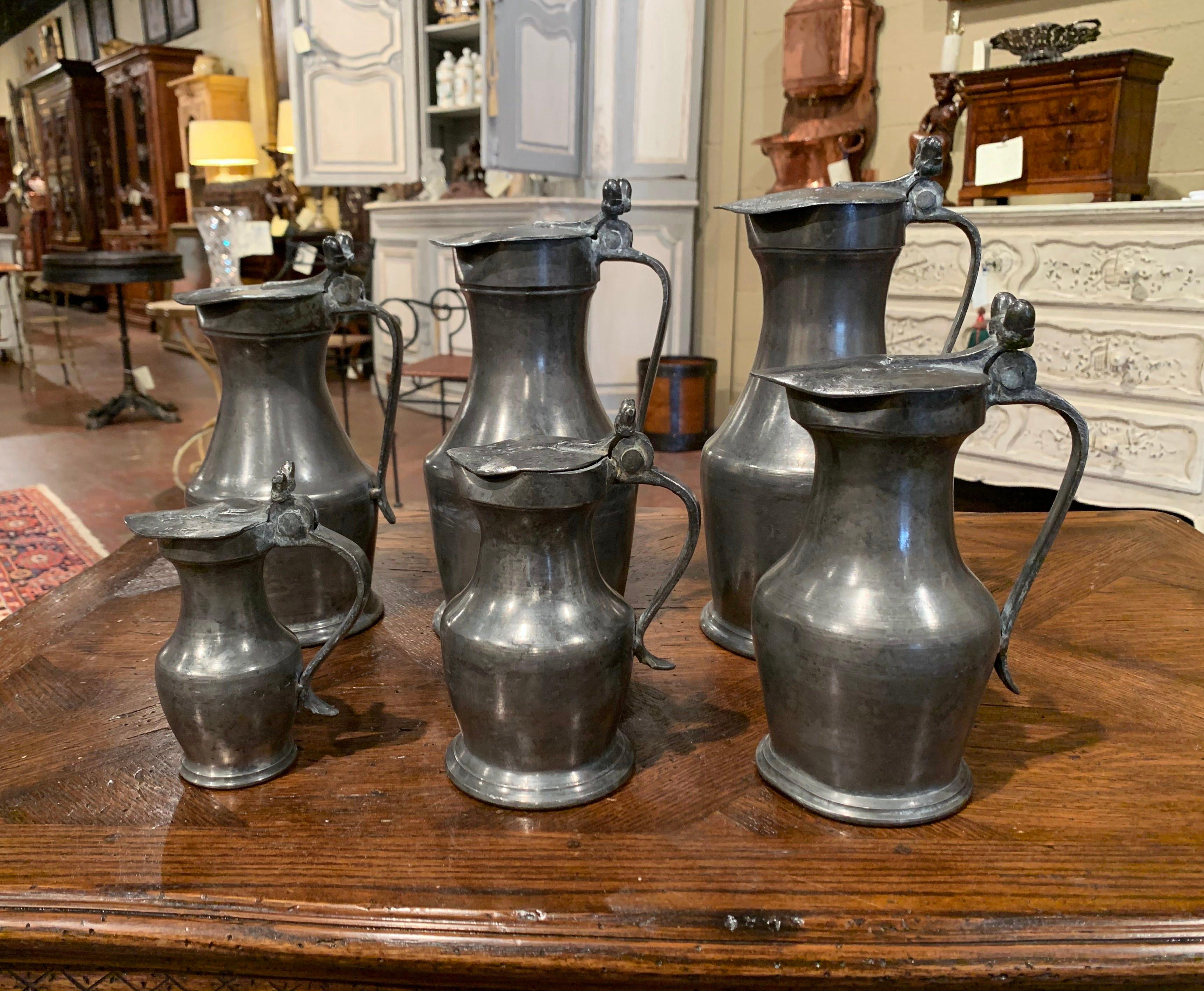 Decorate a shelf or a kitchen counter with this elegant set of antique tankards. Made of pewter, each graduated pitcher has an attached lid decorated with acorns, and a decorative handle, every piece is stamped on the bottom, and is in excellent