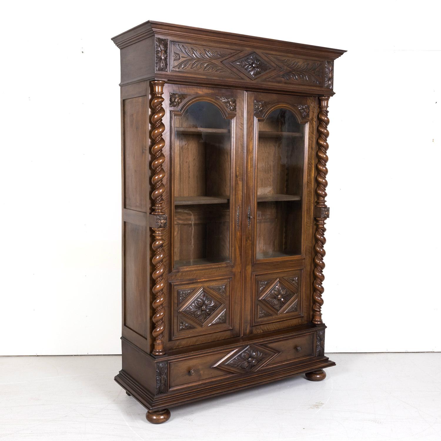 A handsome 19th century French Louis XIII style carved barley twist bibliothèque or bookcase handcrafted in Lyon of solid walnut, circa 1890s, having a stepped cornice over a carved frieze above a pair of three-quarter glass paneled doors with