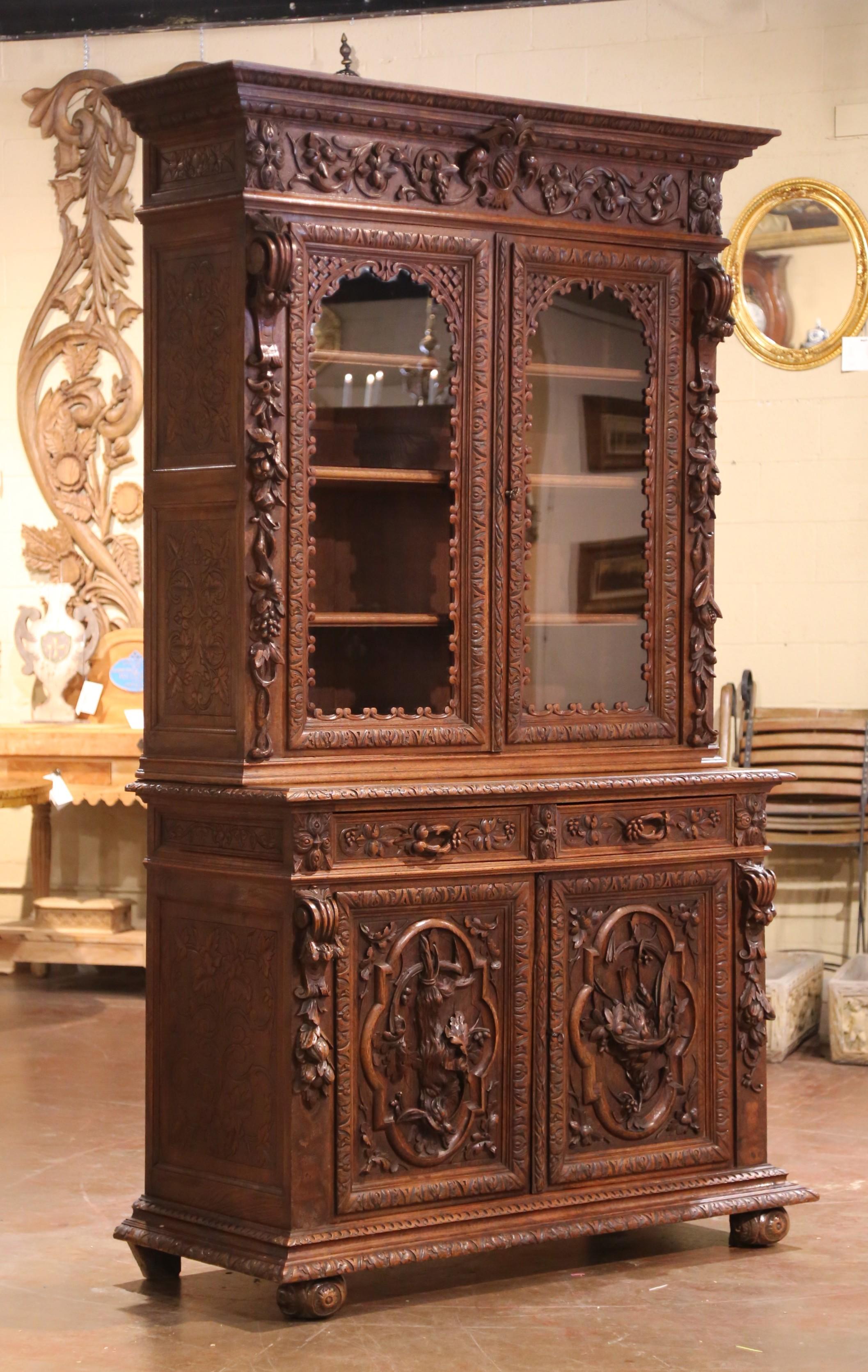 Crafted in France circa 1870, this large two-piece Hunt bookcase exemplifies the Louis XIII style with its richly carved oak façade and commanding presence. Measuring 93 inches high by 57 inches wide and 21.5 inches deep, the cabinet features upper