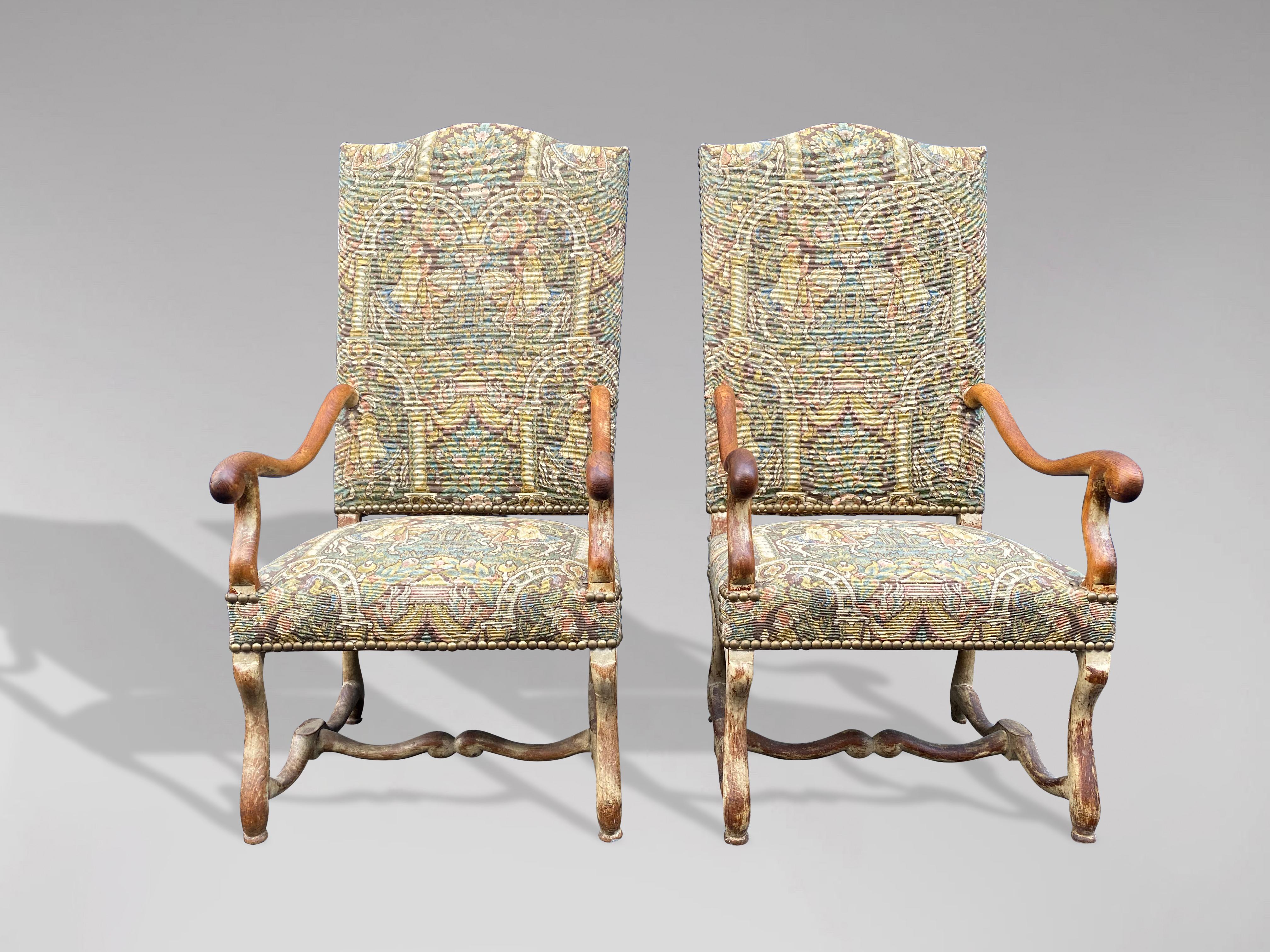 A pair of late 19th century French Louis XIII style walnut os de mouton armchairs or fauteuils, with slanted camelbacks, large scrolling arms, cross stretchers. Each armchair features a tall, slightly slanted camelback, connected to two large