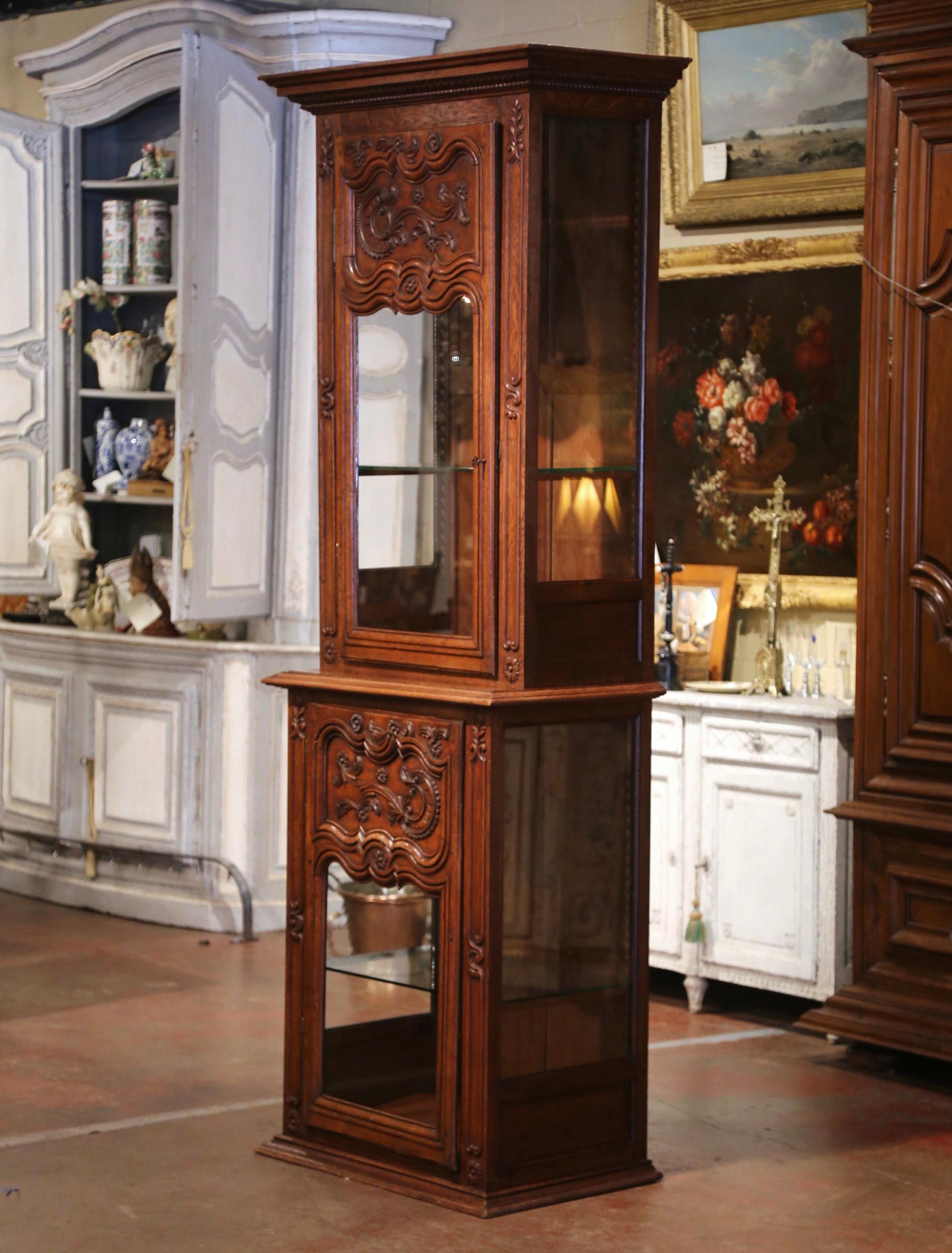 Hand crafted in Normandy, northern France circa 1870, and built in two sections, the antique oak and glass cabinet stands on a thick bottom plinth, and dressed at the pediment with a large carved decorative cornice. Each section features side glass