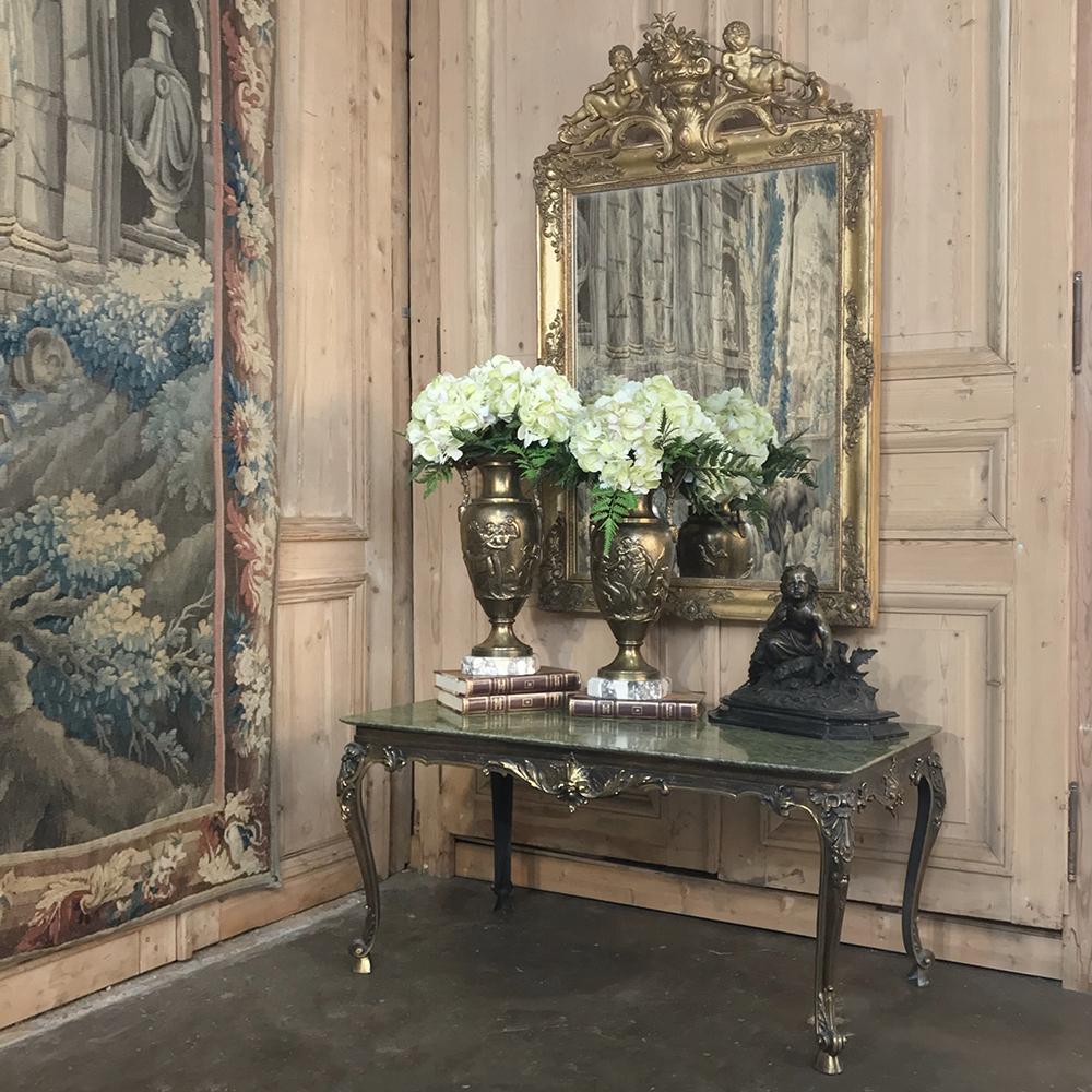 19th century French Louis XIV Gilded Mirror is a delight to behold, with an intricately detailed frame crowned with two reclining cherubs on each side of an urn bursting with a floral bouquet. Featuring its original gilded finish, it is an artful