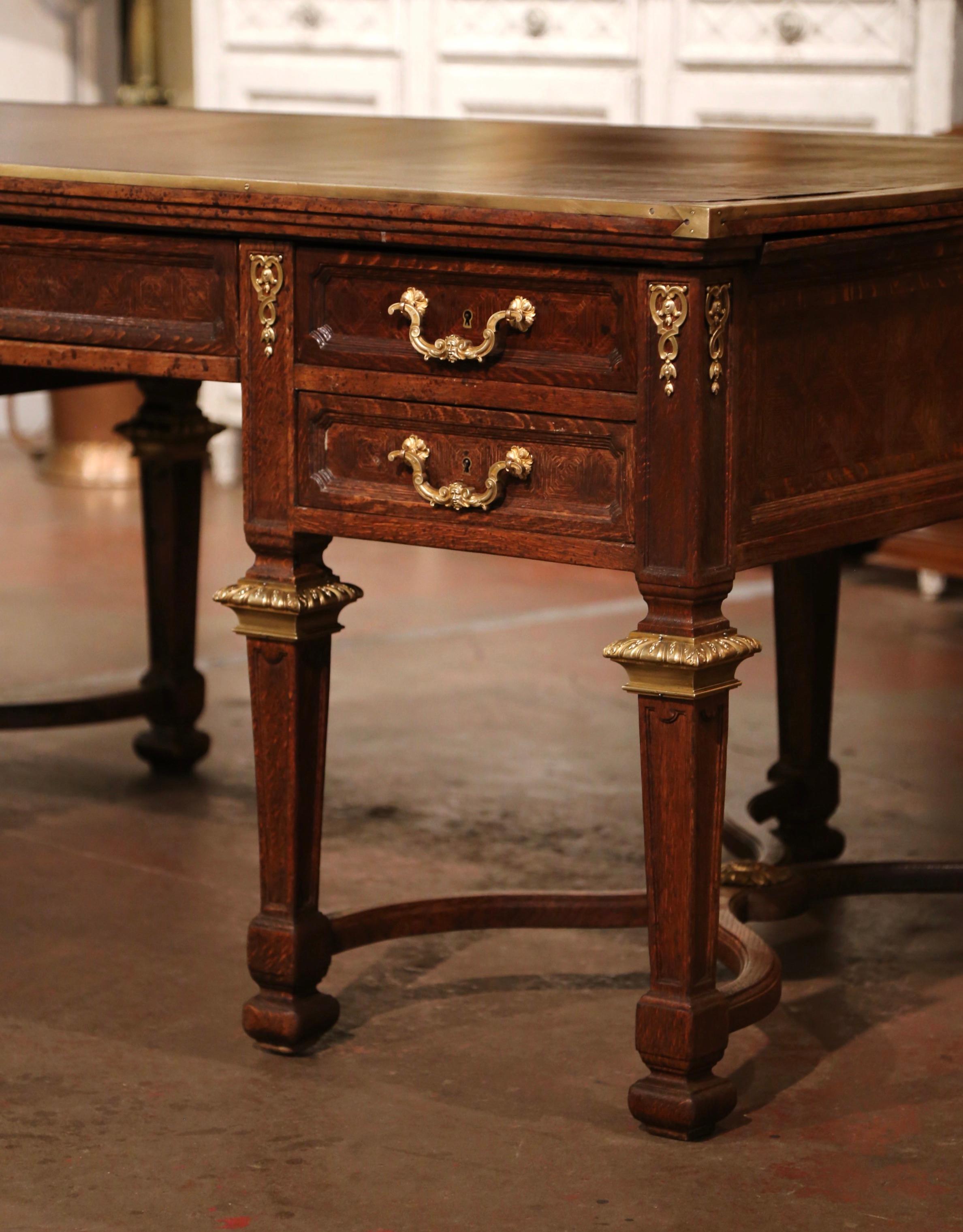 This elegant antique oak desk was crafted in northern France circa 1840. Standing on eight squared and tapered legs decorated with bronze mounts at the shoulder, and connected with double X stretcher at the base, the large writing table is decorated