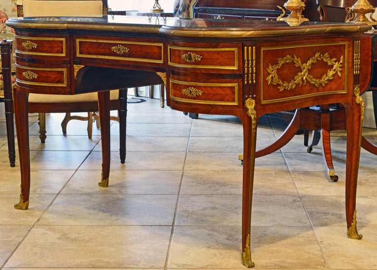 This exceptional French Louis XV style kingwood parquetry writing desk or bureau plat features a parquetry inlaid top protected by shaped glass above a central bronze trimmed frieze drawer flanked by two circle segment front sections with two