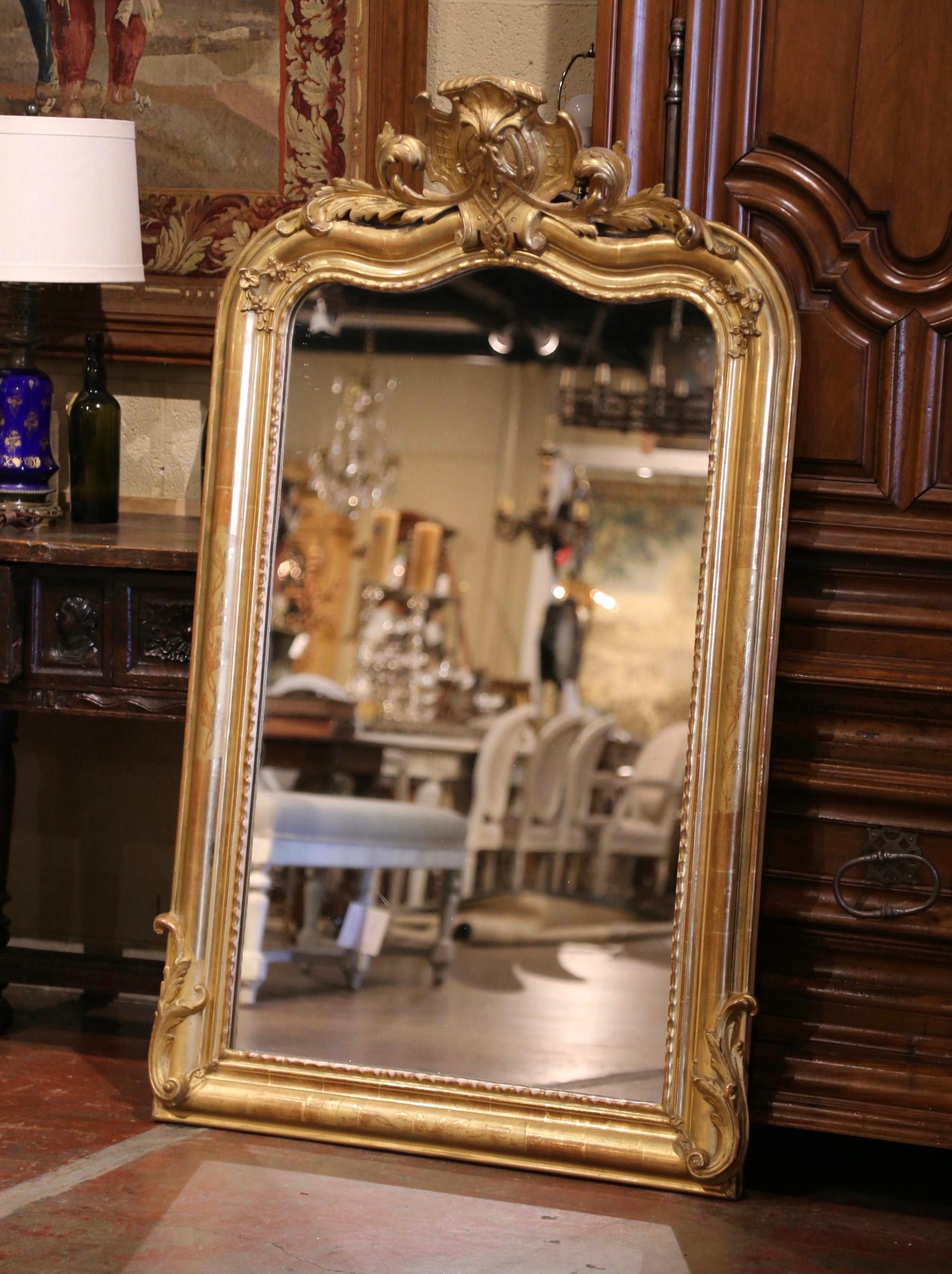 Con casi metro y medio de altura, ¡este importante espejo dorado antiguo es único en su especie! Fabricado en París, Francia, hacia 1870, el espejo alto con parte superior arqueada y serpentina está decorado en el frontón con una gran cartela de