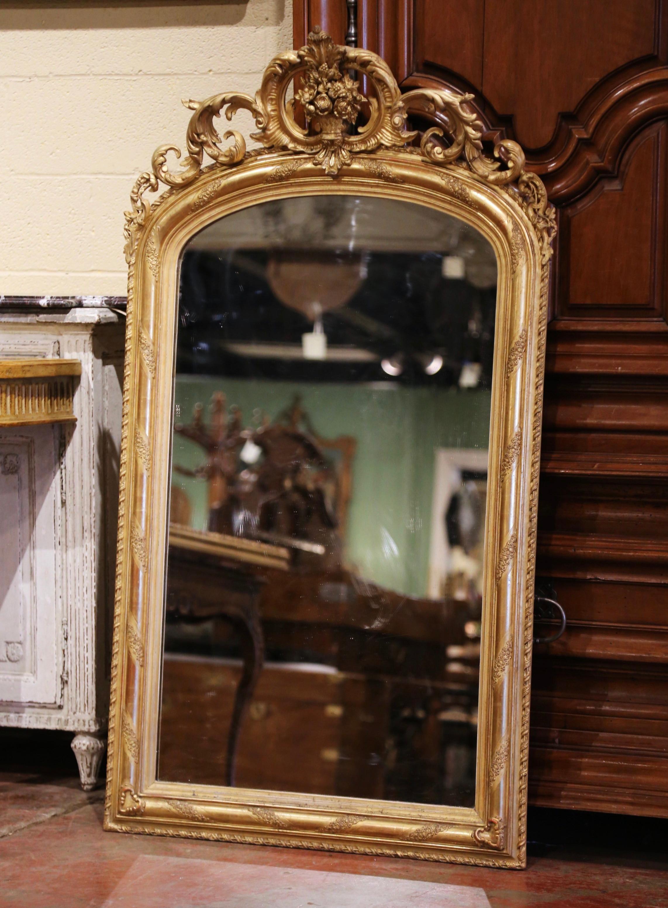 This elegant antique mirror was crafted in France, circa 1870. Arched at the top, the ornate pediment features a floral decor cartouche with leaves on the sides and the frame is decorated with foliage motifs throughout. The Louis XV mirror has the