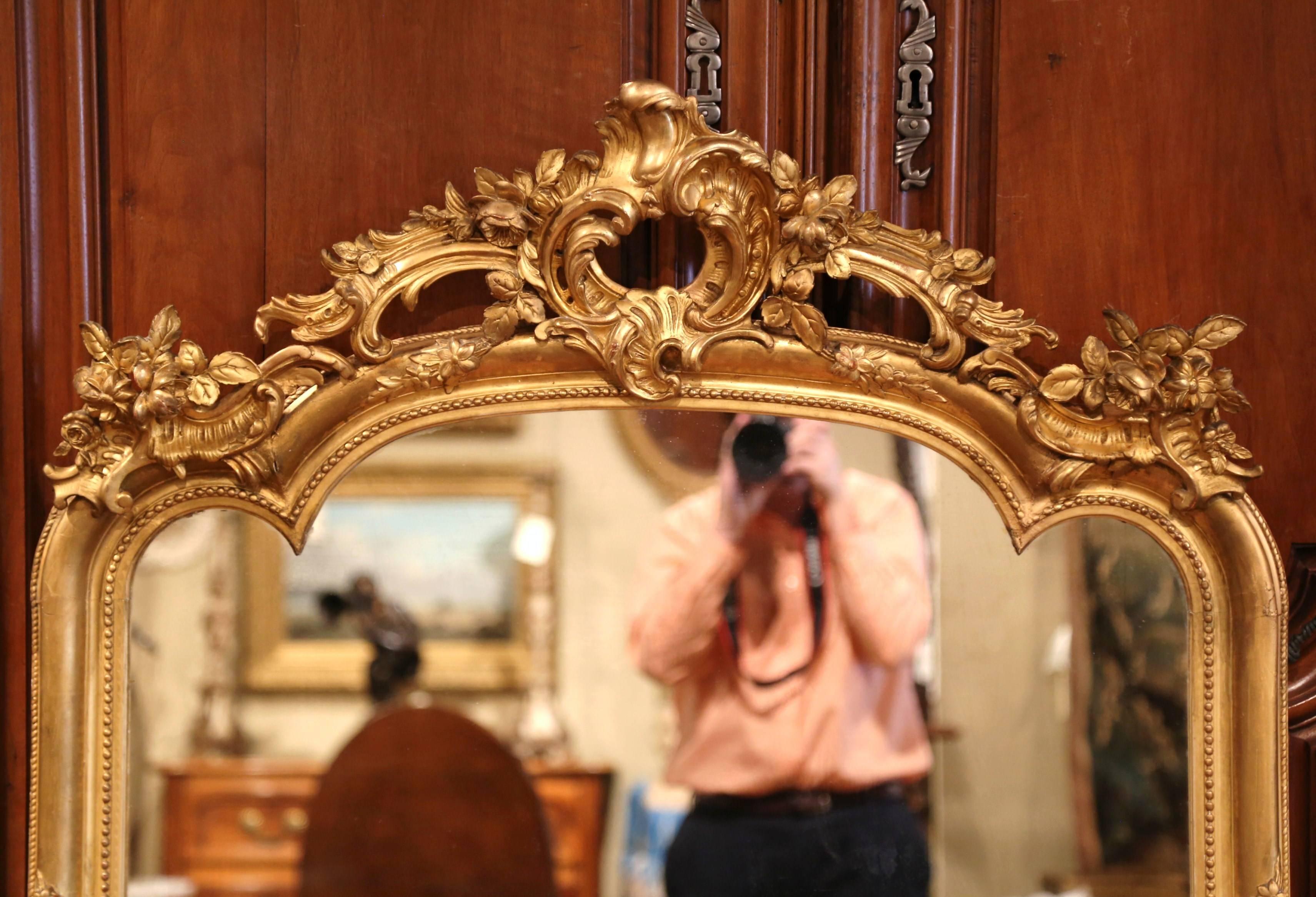 This elegant, antique wall mirror was crafted in Paris, France, circa 1870. The mirror has a curved top and features an intricate frame. The carved pediment has a large shell motif in the center, with flowers and leaves on both sides. Both sides