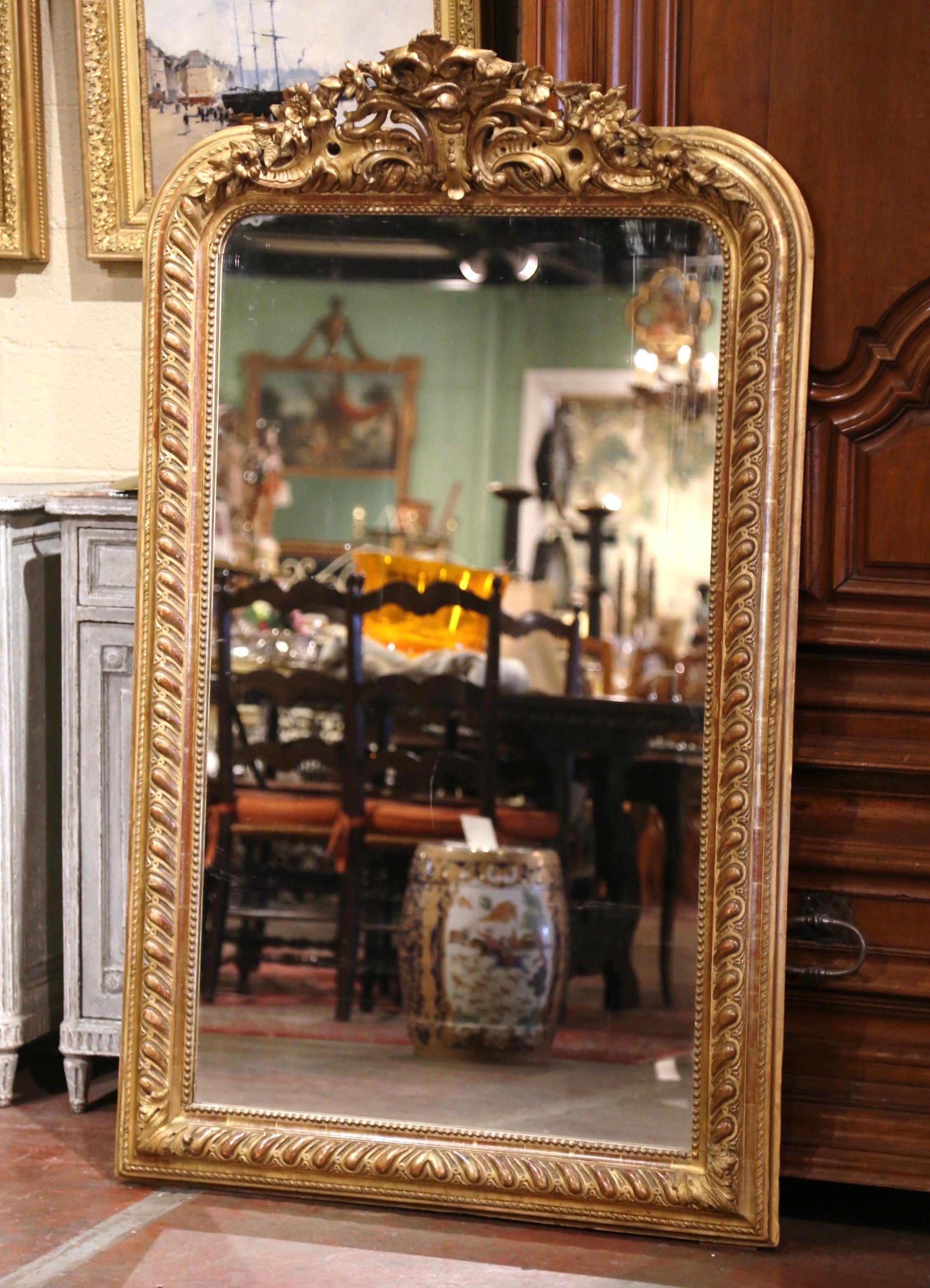 Over five and a half feet tall, this important antique mirror is a one of a kind! Crafted in Paris, France circa 1850, the grand mirror is decorated with a hand carved cartouche at the pediment featuring floral and foliage motifs in high relief. The