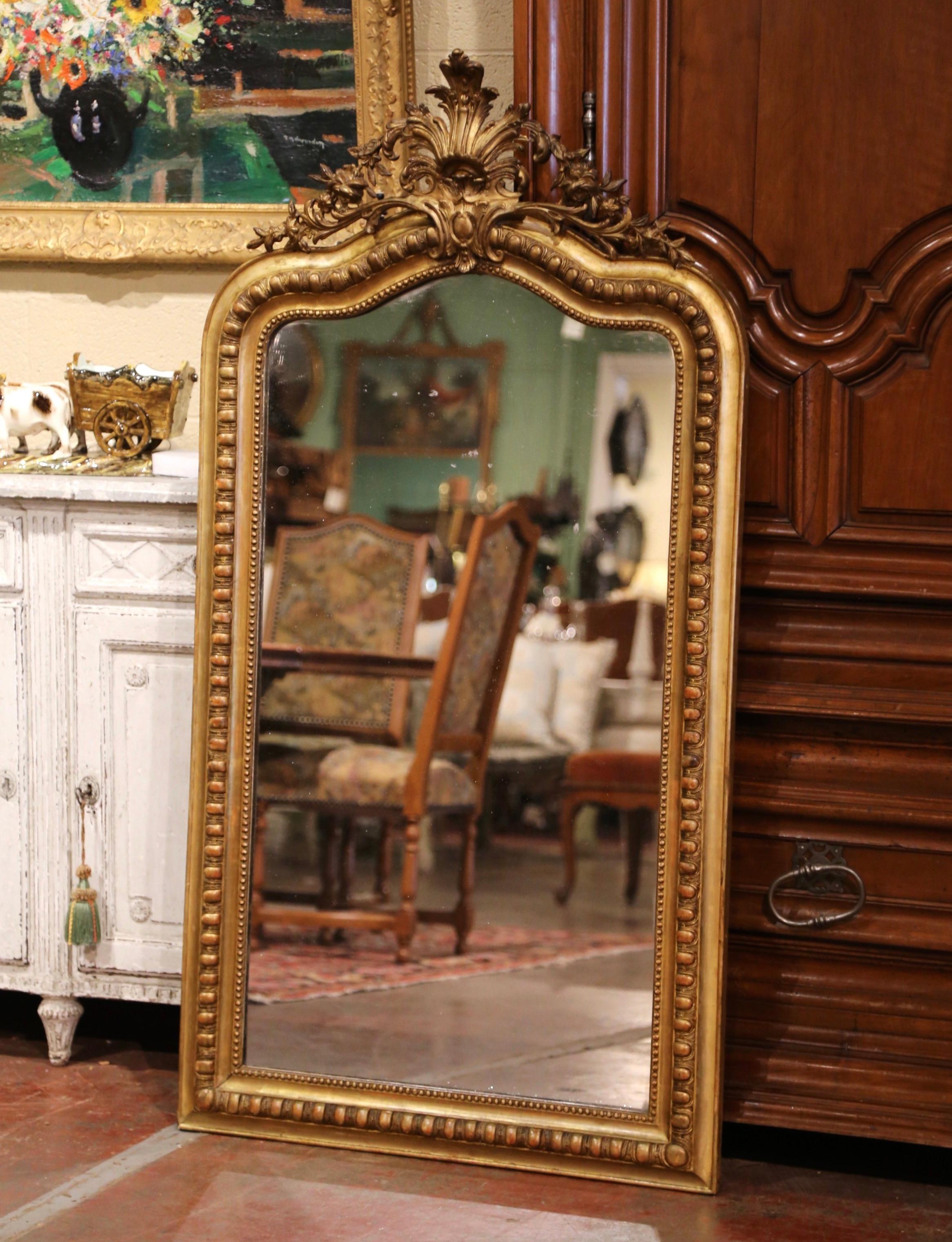 This elegant antique gilt mirror was crafted in France, circa 1870. Arched at the top, the ornate pierced pediment features a floral and shell decor cartouche with leaves trailing down the sides and the frame is decorated with geometric designs