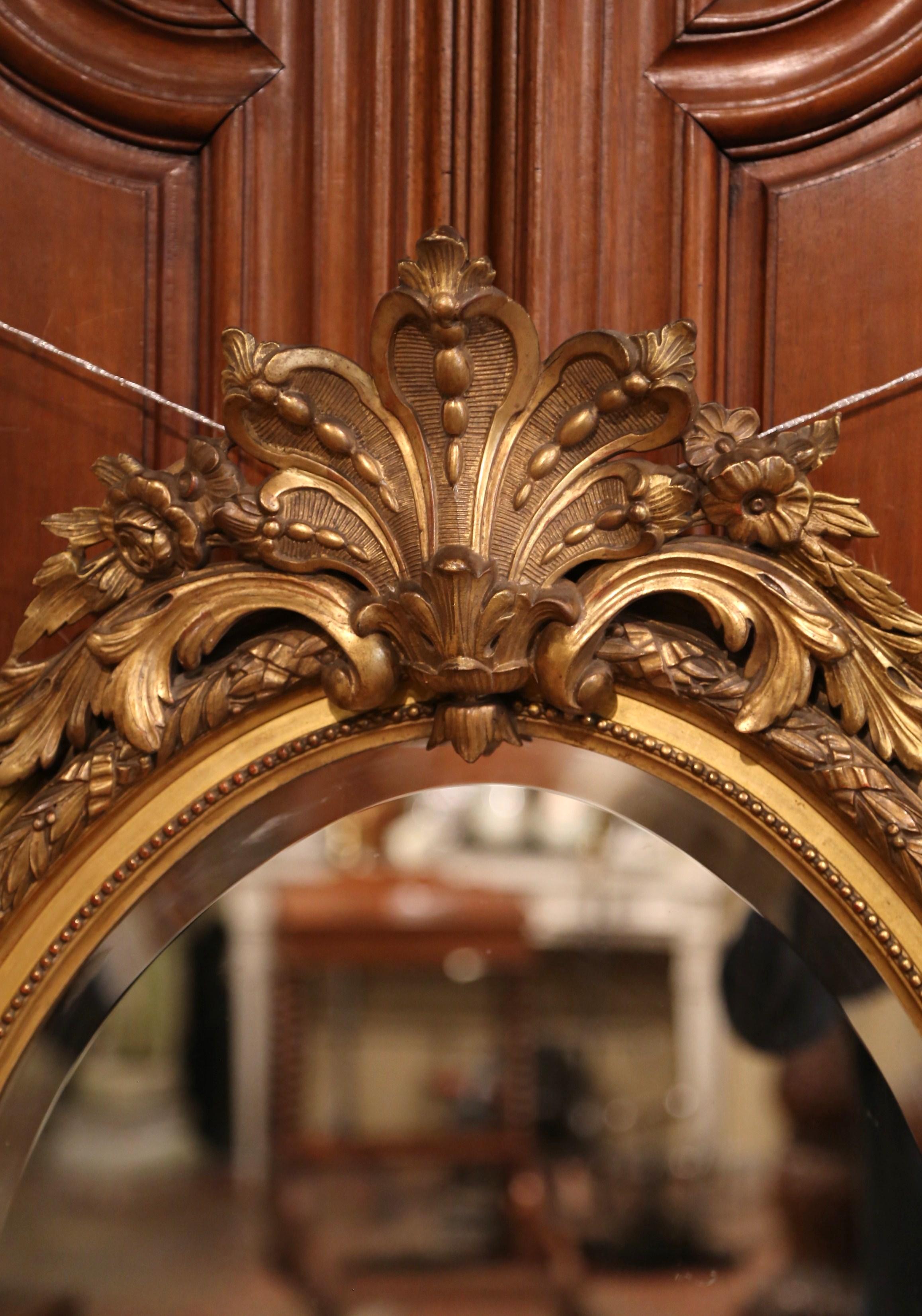 This elegant, antique wall mirror was created in France, circa 1870. The feminine, oval mirror features a decorative shell cartouche flanked with foliage and floral decor, intricate carvings around the frame and leaf decor with central medallion at