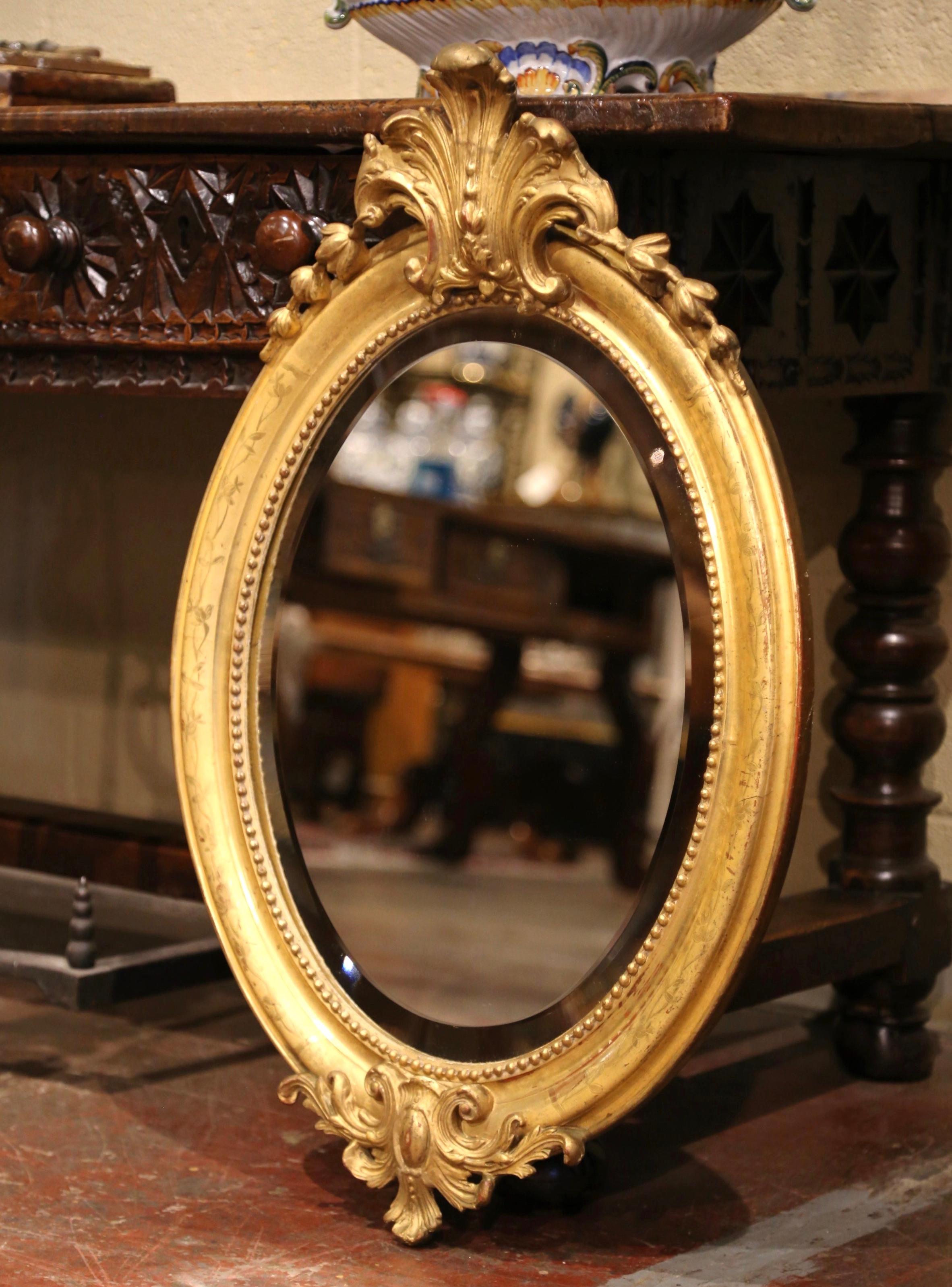 This elegant antique gilt mirror was created in France, circa 1870. Oval in shape, the mirror features a decorative shell cartouche flanked with foliage decor, discrete engraved floral motifs around the frame and another intricate shell motif in