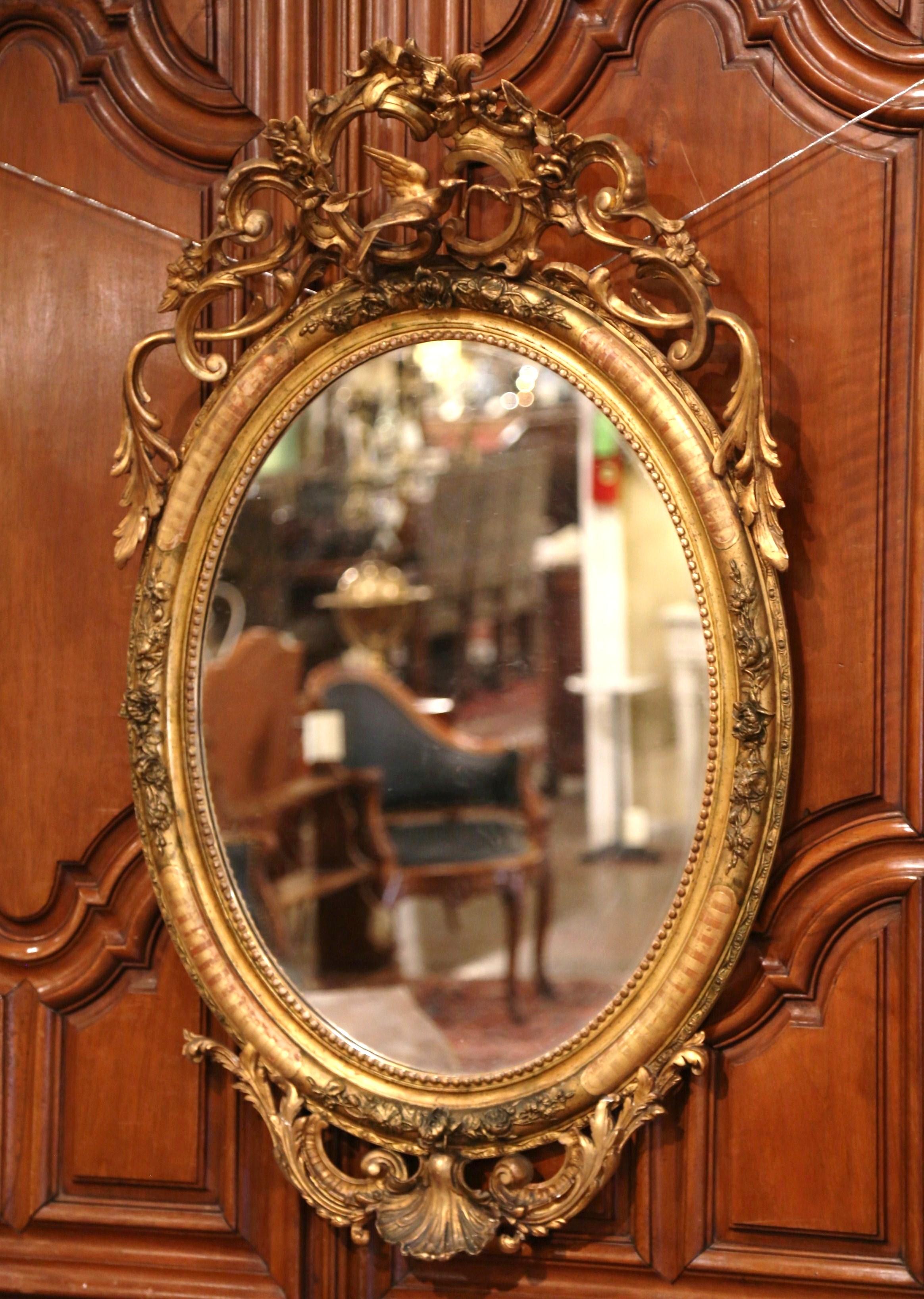 Decorate a powder room or entryway with this elegant antique wall mirror. Crafted in France, circa 1860, the beaded oval frame is decorated with floral motifs including a carved bird cartouche at the pediment, and embellished with shell and leaf