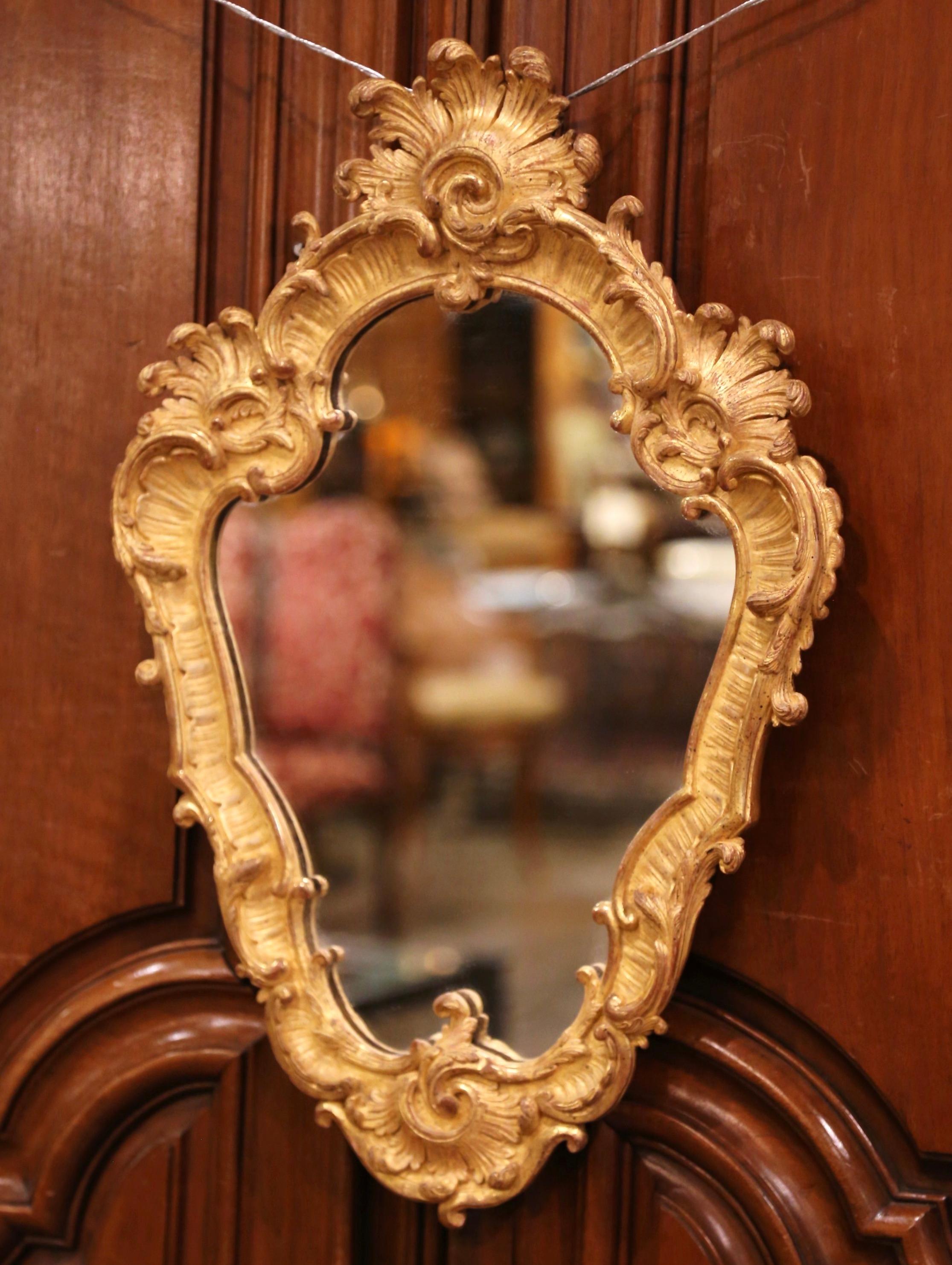 Crafted in France circa 1880, the elegant antique gilt mirror in the Louis XV style, features gracious lines with intricate carving, including scrolled and foliage decor, and embellished with a carved shell cartouche at the bottom. The petite Rococo
