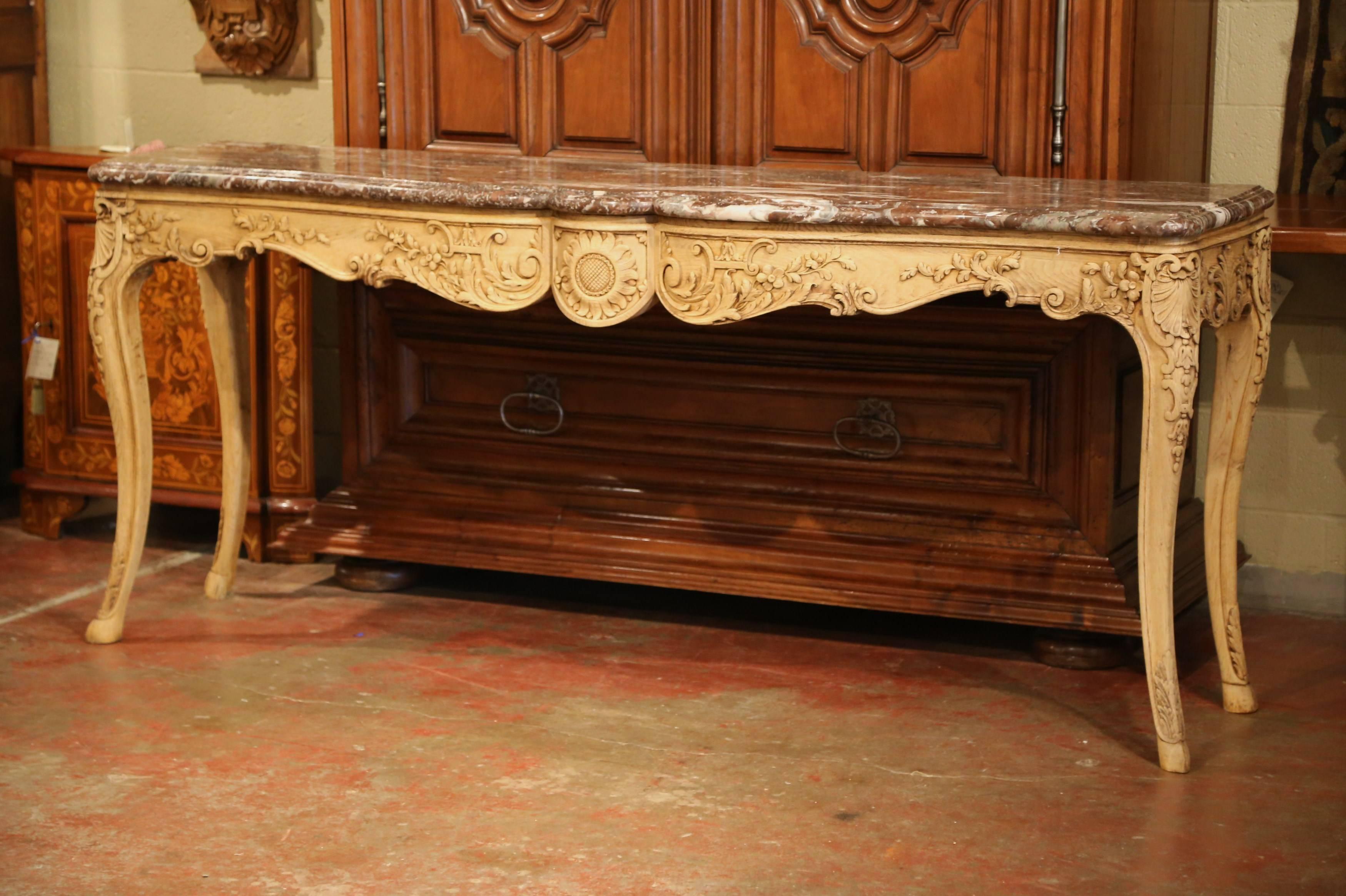 This elegant, antique console was crafted in Lyon, France circa 1880. Carved of oak, the console table features a serpentine shaped marble top on a conforming base. The scalloped apron has a center carved sunflower flanked by scrolling acanthus leaf
