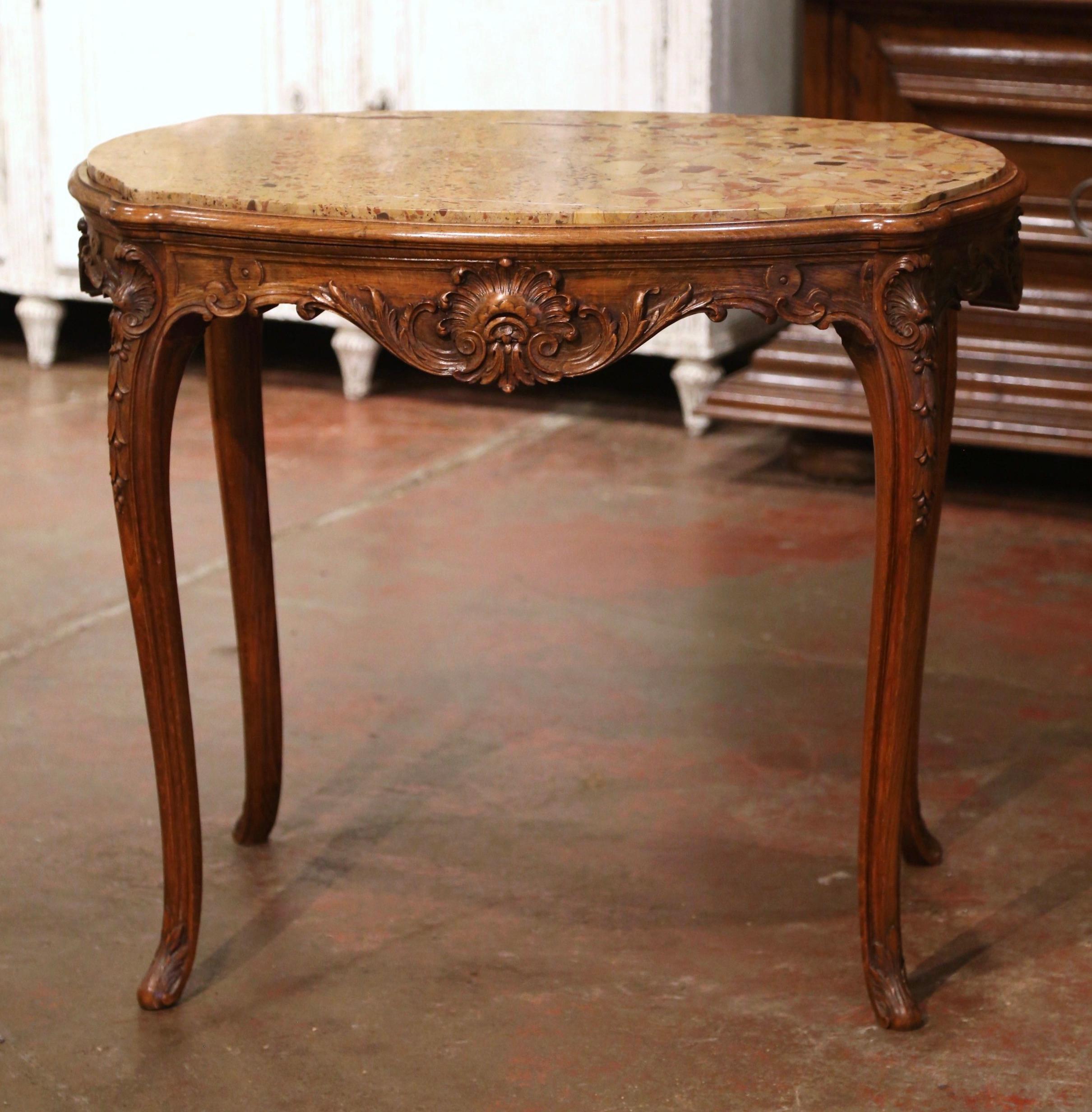 Crafted in France, circa 1880 and oval in shape, the antique table stands on cabriole legs ending with acanthus leaves at the feet. The elegant end table is decorated with delicate hand carved shell and foliage motifs around the scalloped and bombe